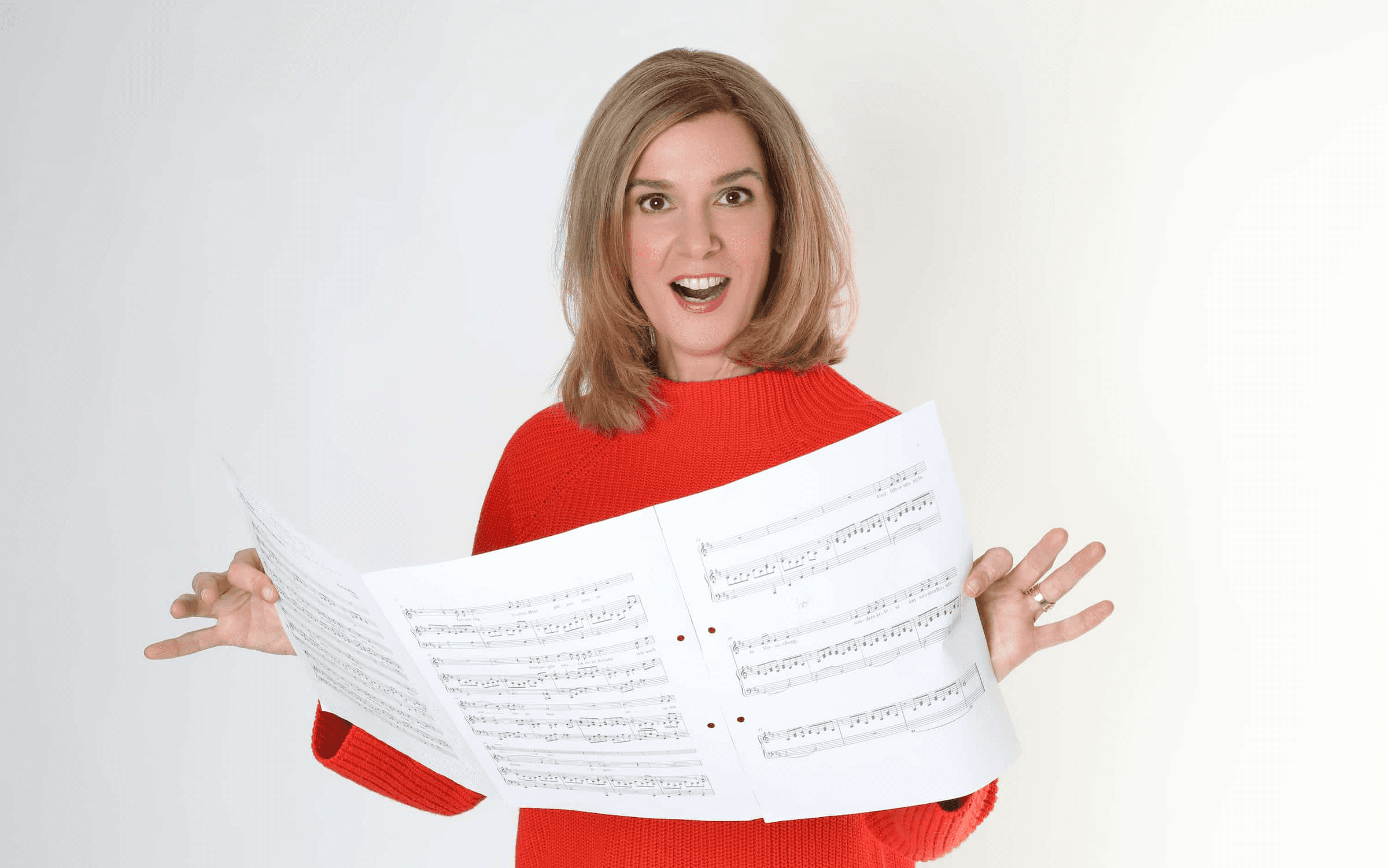 Danielle Zuber singt freudig und hält Notenblätter in der Hand. Promotion für den Online-Gesangskurs 'Singen lernen in 30 Tagen' von Singers Evolution.