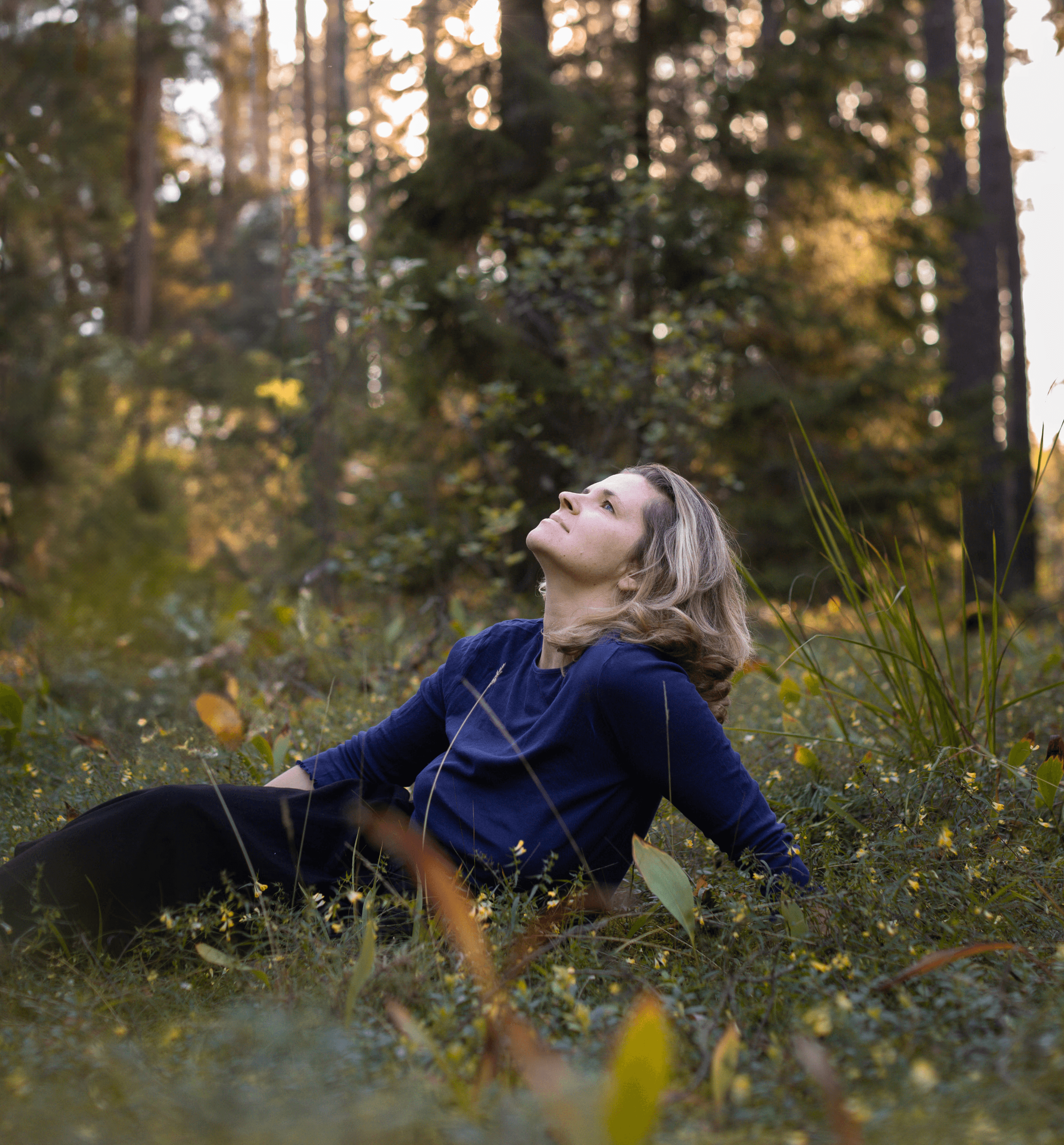 Kobieta siedząca w trawie na skraju lasu patrząca w niebo