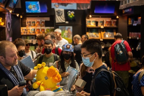 Visiteurs pressés autour d'un stand Ankama sur un salon, peluches et artbooks en vitrine