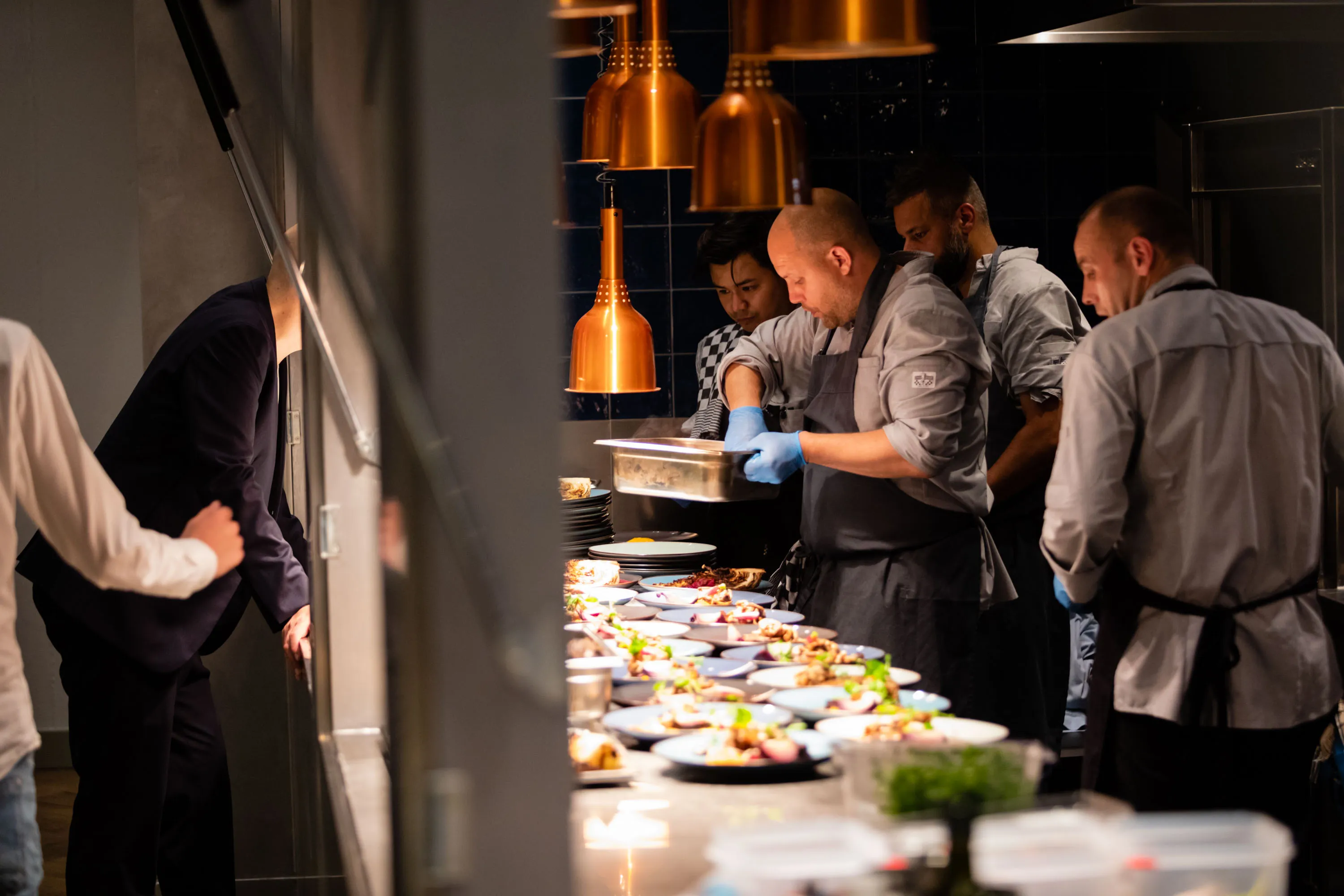 A group of chefs collaborates in a busy kitchen, preparing dishes at a countertop filled with ingredients.