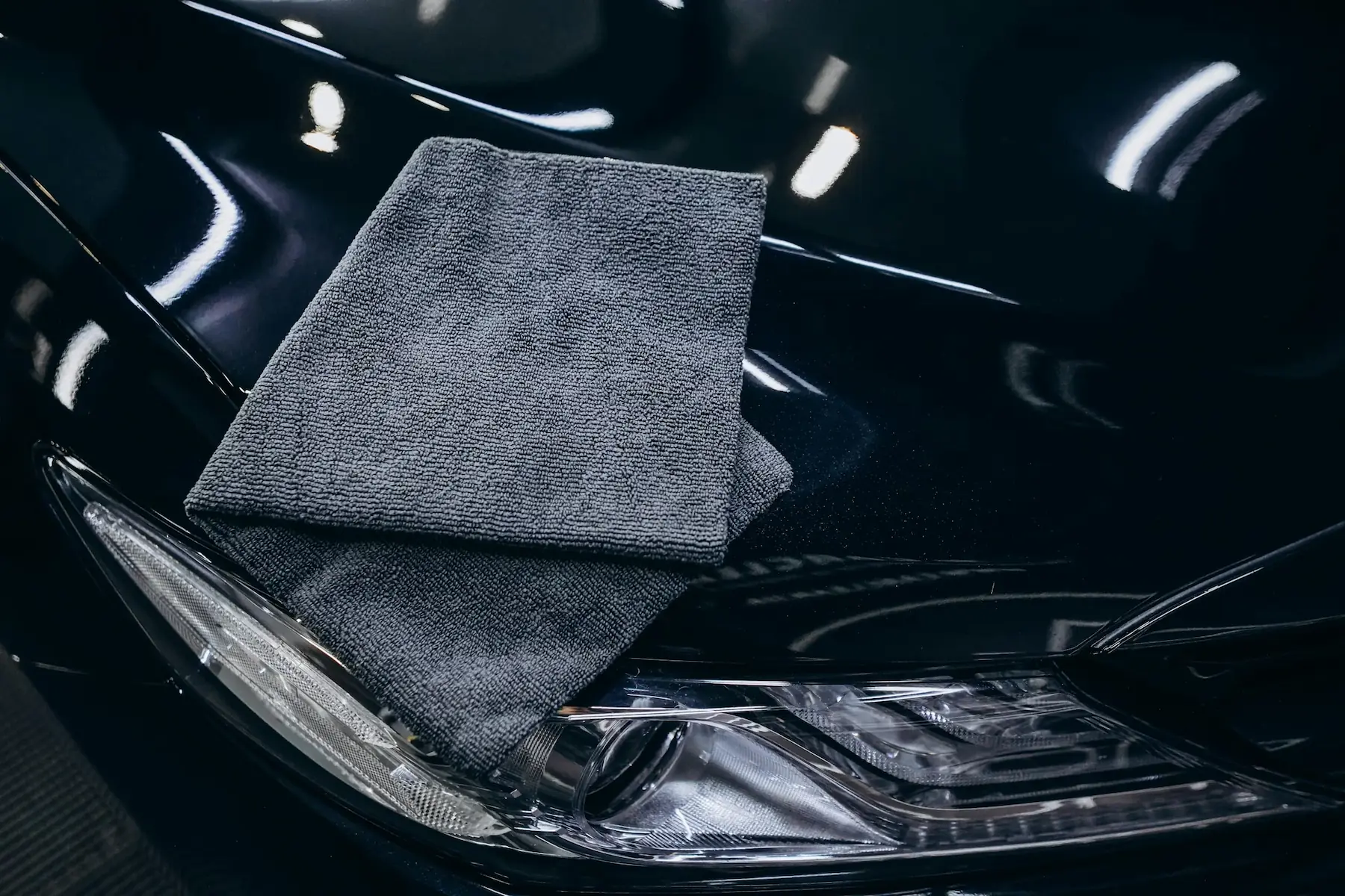 Microfibre posée sur la carrosserie noire d’une voiture lors d’un detailing automobile