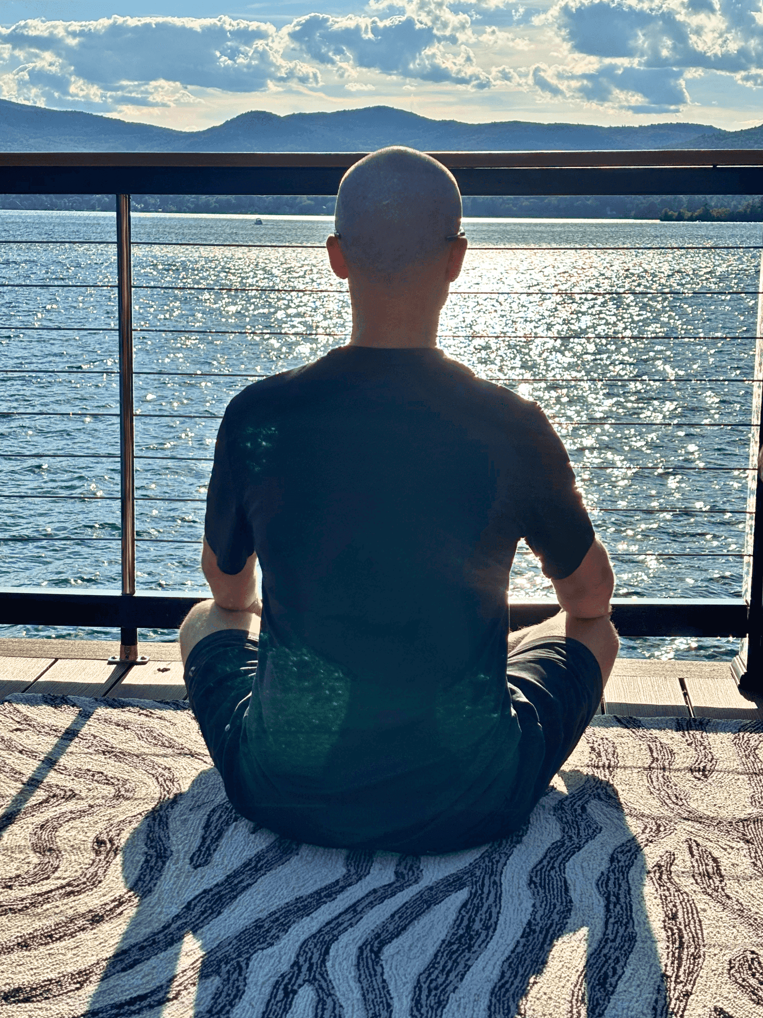 man meditating on a dock by the lake during sunset