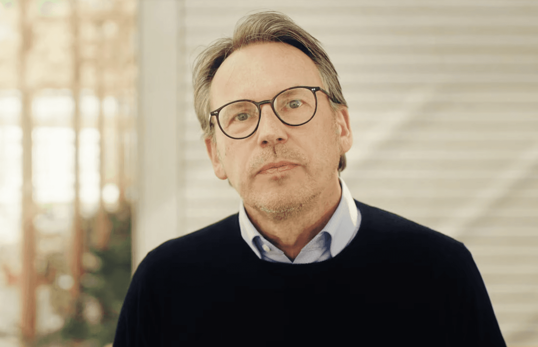 Young woman smiling gently in natural sunlight, with warm shadows cast across a minimal background.