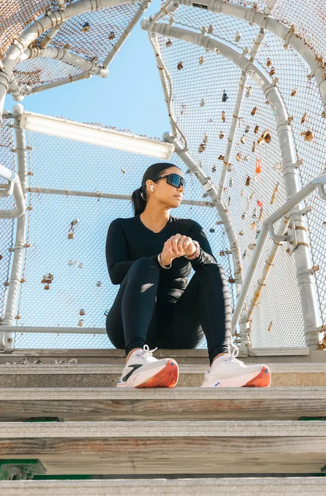 Woman resting after a workout in sunlight, wearing sportswear and sunglasses