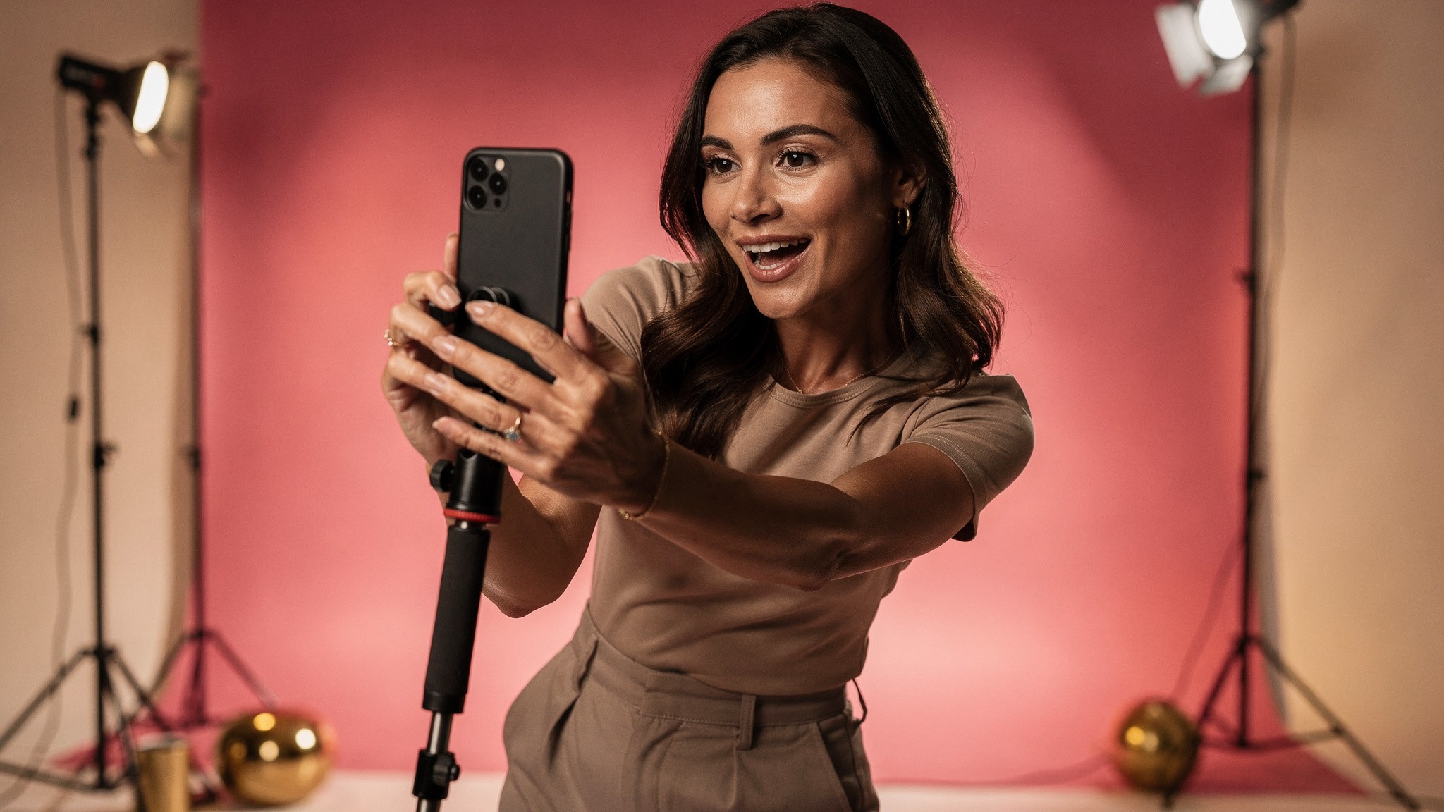 Adult woman creator filming a vertical video on a handheld phone setup in a studio