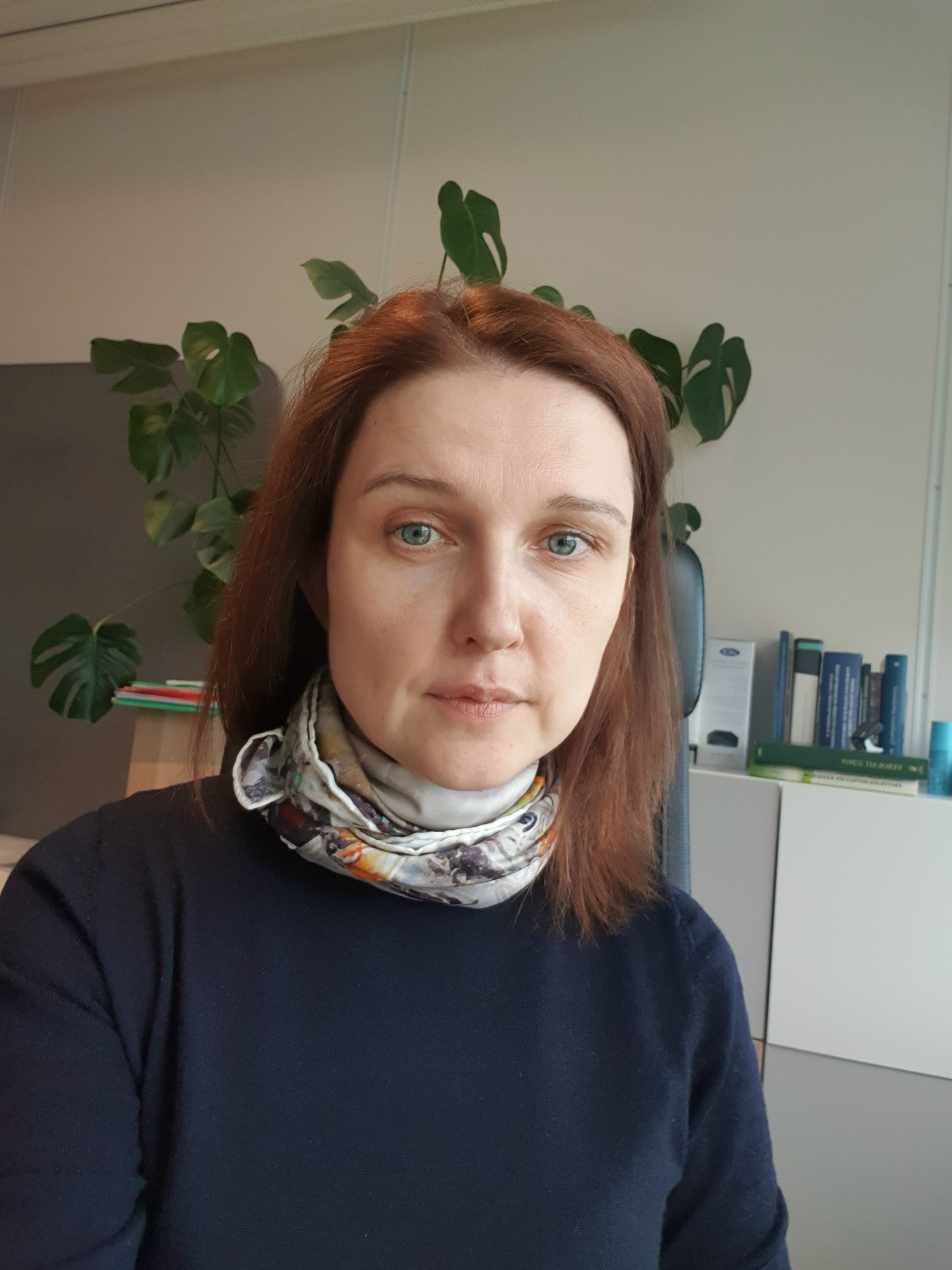 A man wearing glasses and a blazer working at a desk, writing in a notebook beside a computer monitor in a modern office.