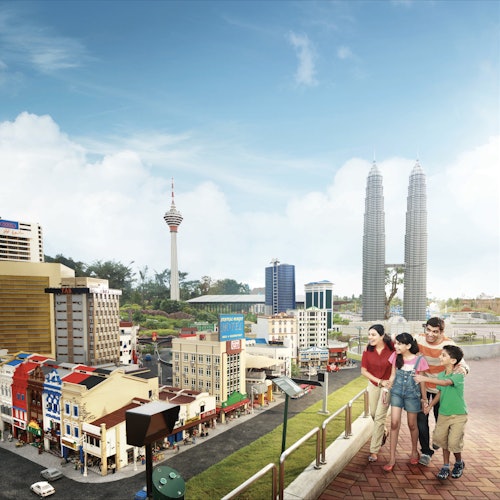 A family of four admires a miniature cityscape, featuring detailed buildings and iconic towers under a bright blue sky.
