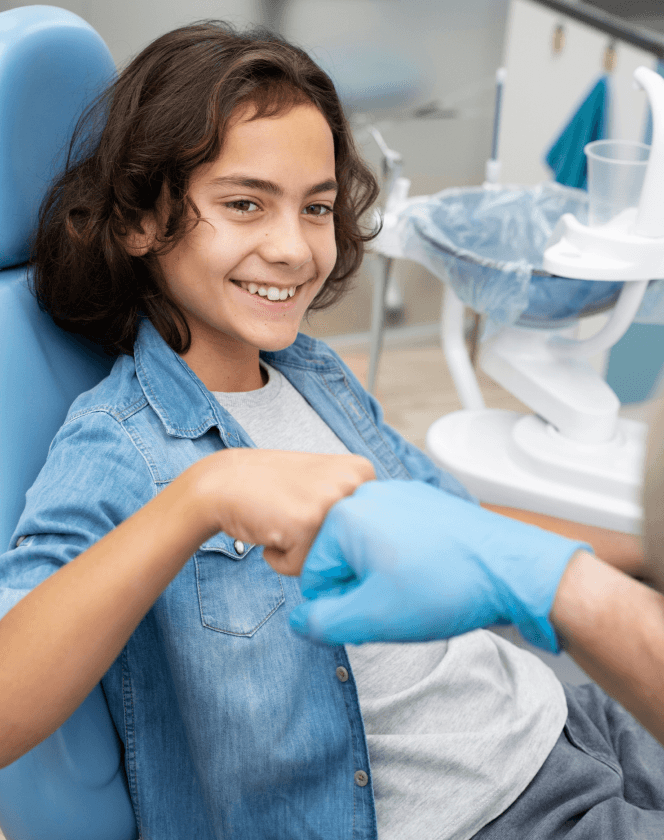 A dentist and a young female patient smiling, with the patient holding a mirror to examine her teeth.