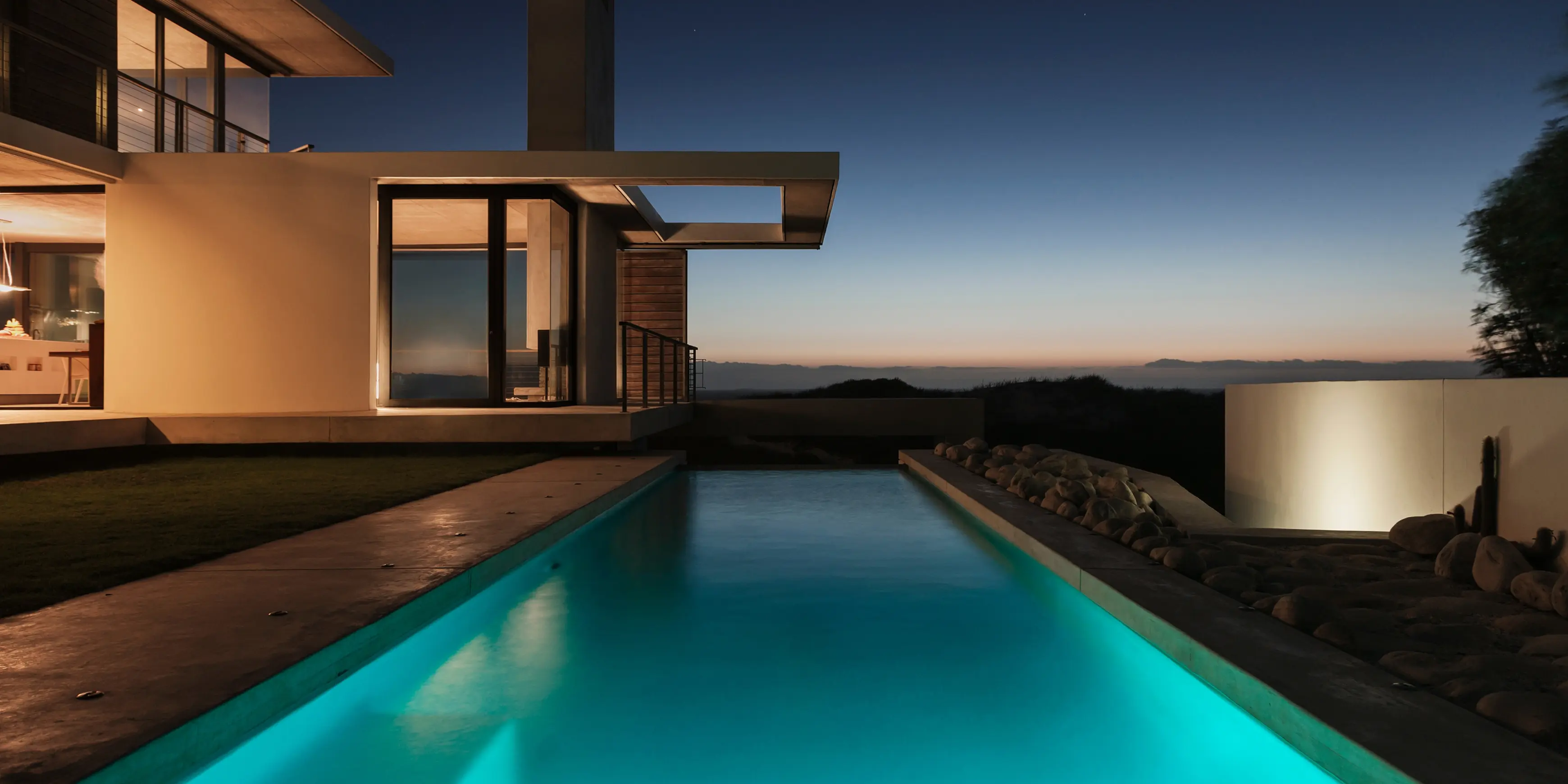 A stunning image of a pool next to a modern house at sunset