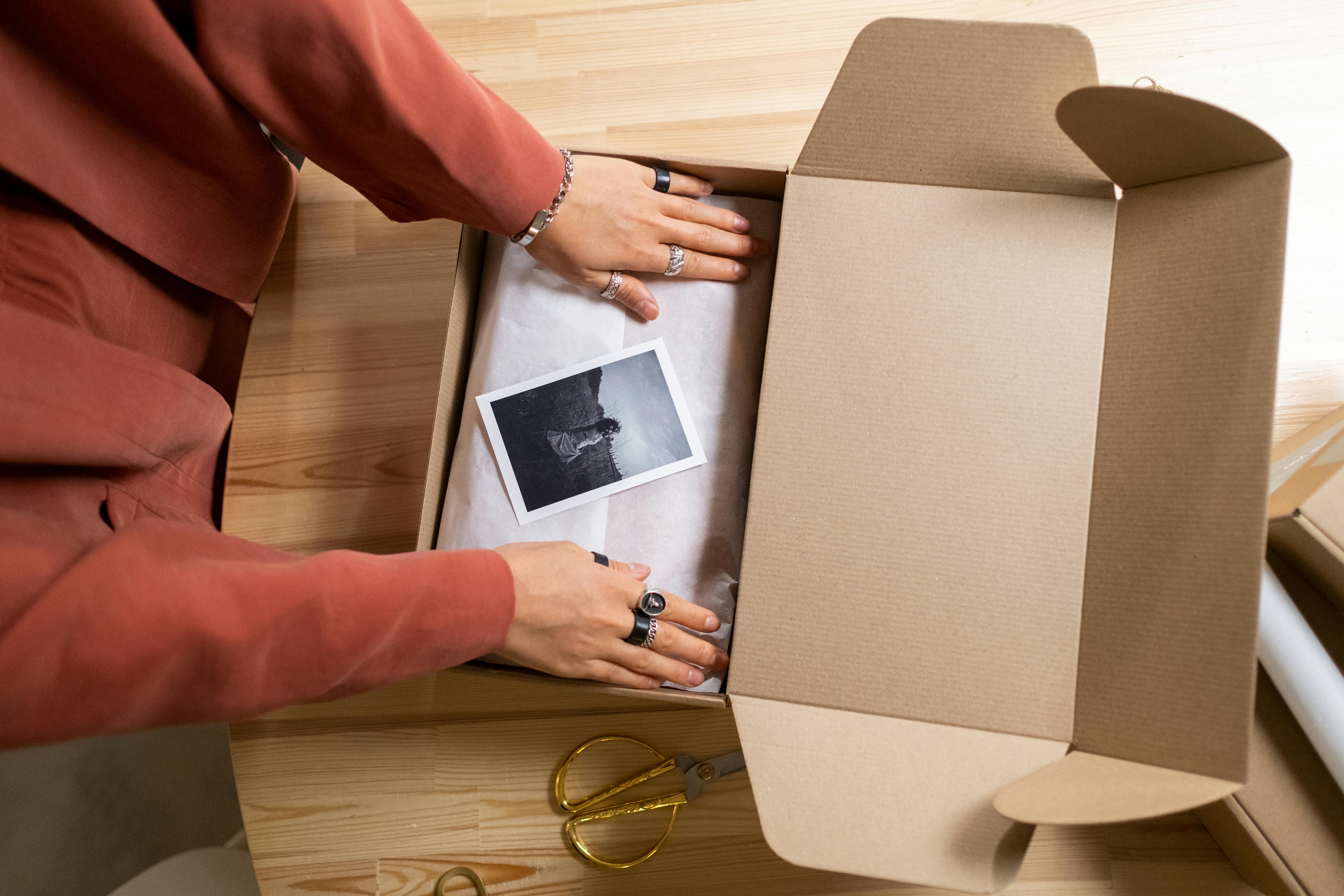 A person's hands are opening a cardboard box for giveawayto reveal a small item inside on a wooden surface.