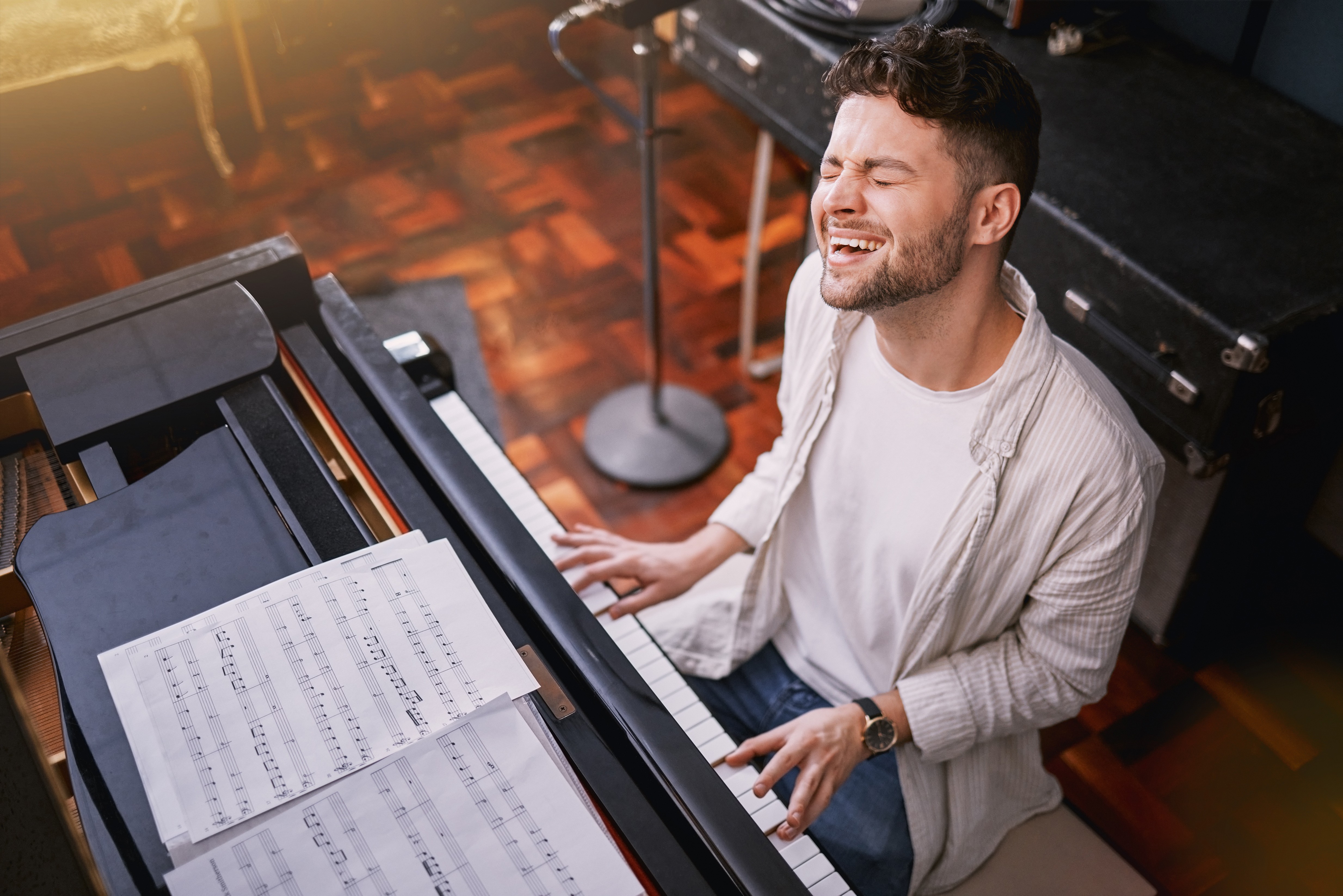 Man sitting at a piano and smiling while engaging with a student during a singing lesson.