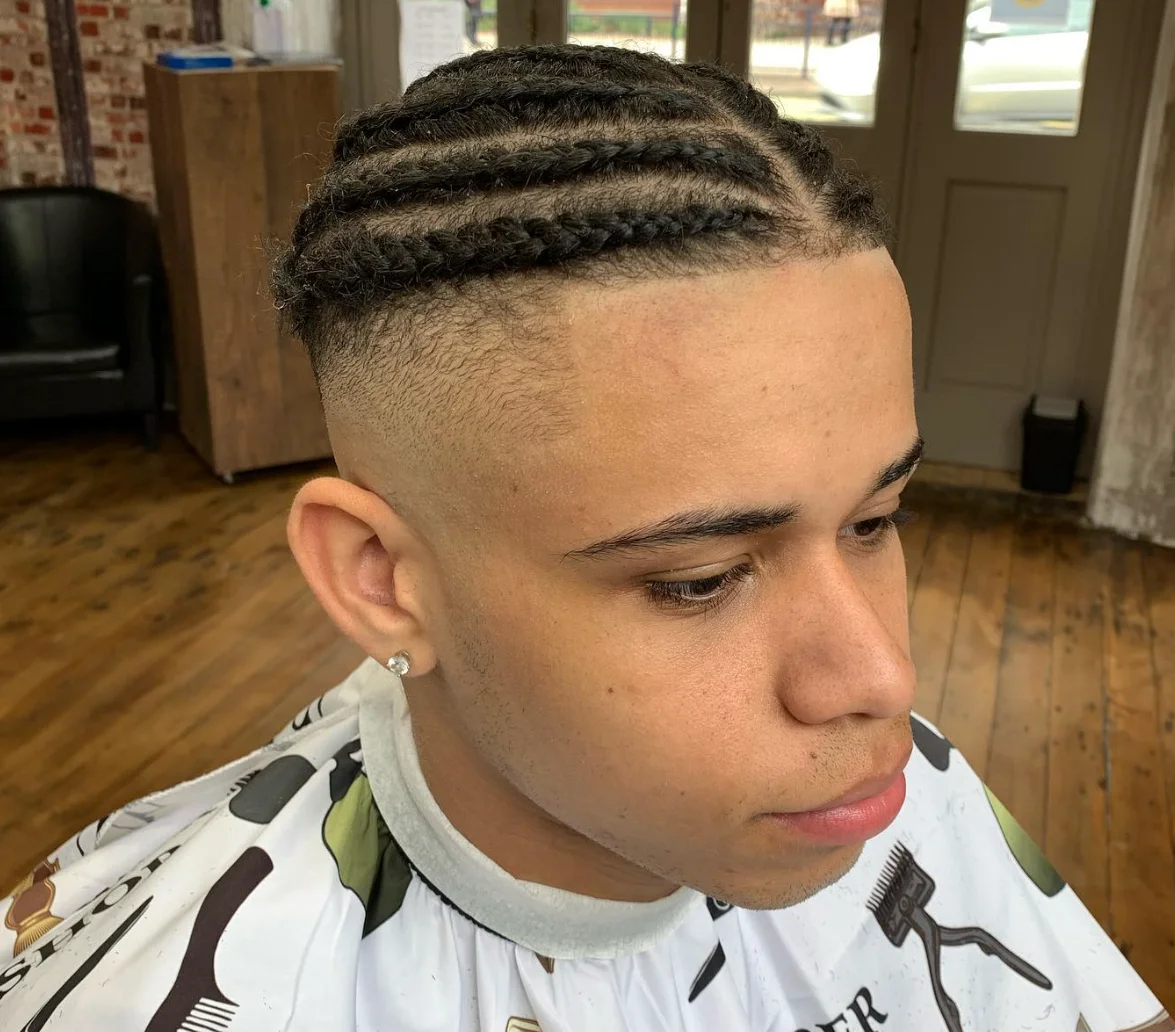 Young man with braids and a taper fade, seated in a premium barbershop