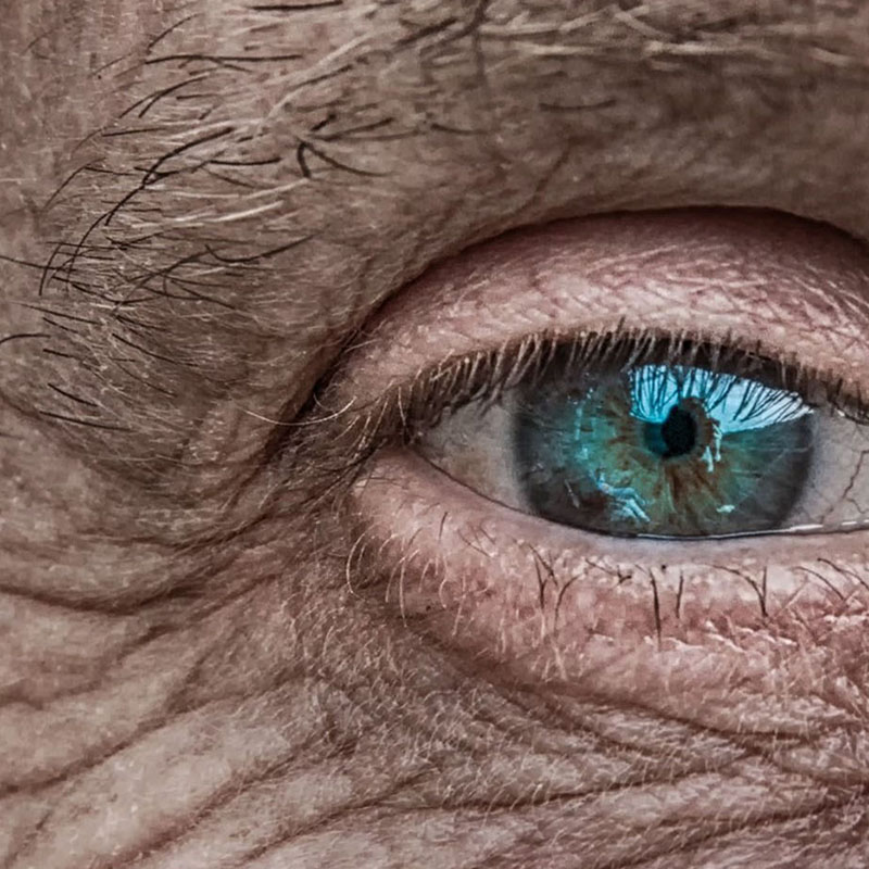 A smiling young man with crossed arms, wearing a plaid shirt and white t-shirt, poses against a dark background.
