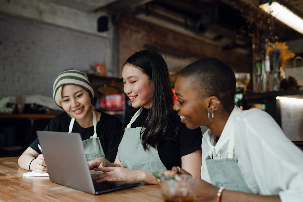 Colegas alegres trabajando juntas en la computadora portátil en la cafetería