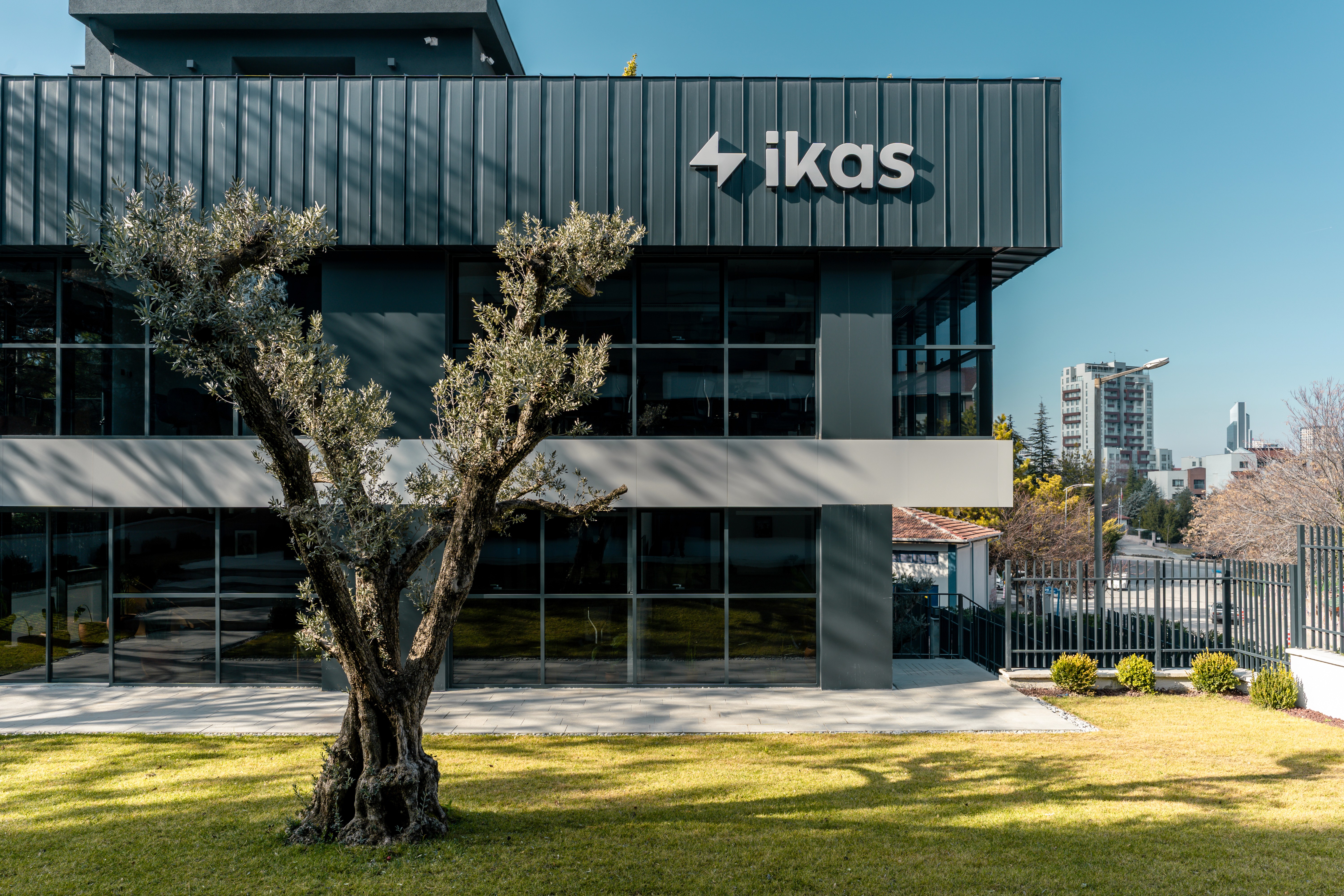 Modern office building with glass façade, metal cladding, and olive tree landscaping — Ikas Headquarters exterior design in Ankara.