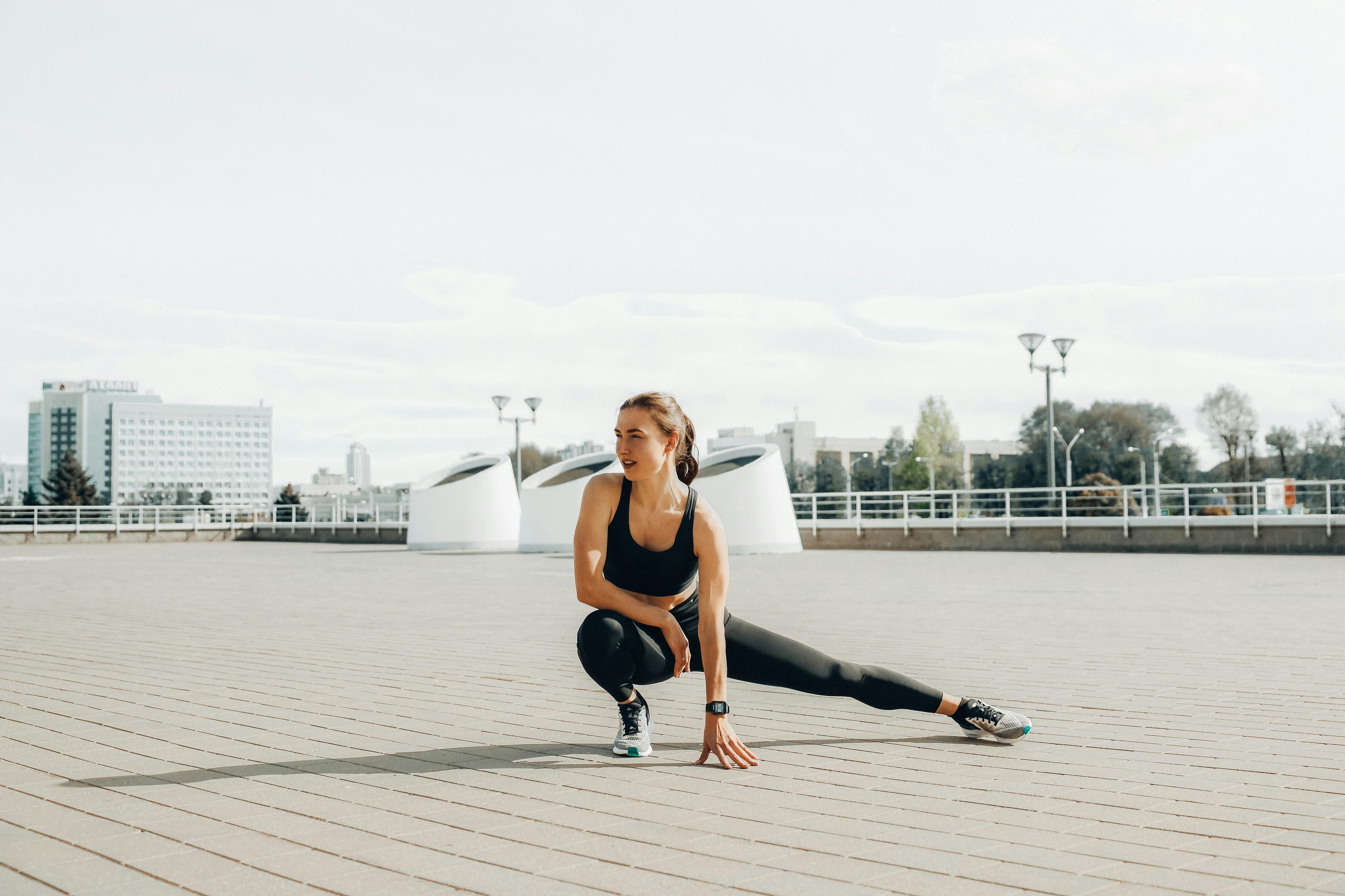 A woman in activewear crouching in an athletic pose in a large, open, urban space