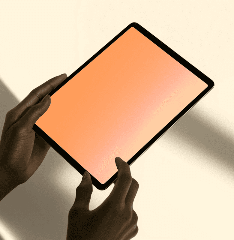 Close-up of hands holding a tablet with an orange gradient screen against a beige background.