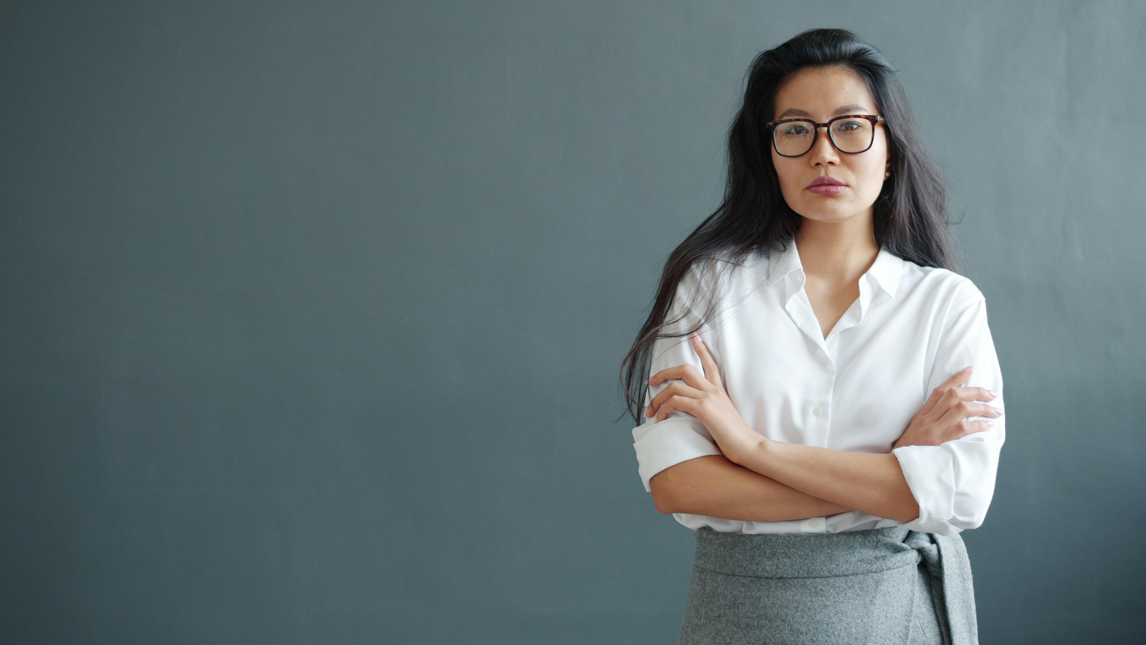 Woman with glasses and arms crossed against gray wall