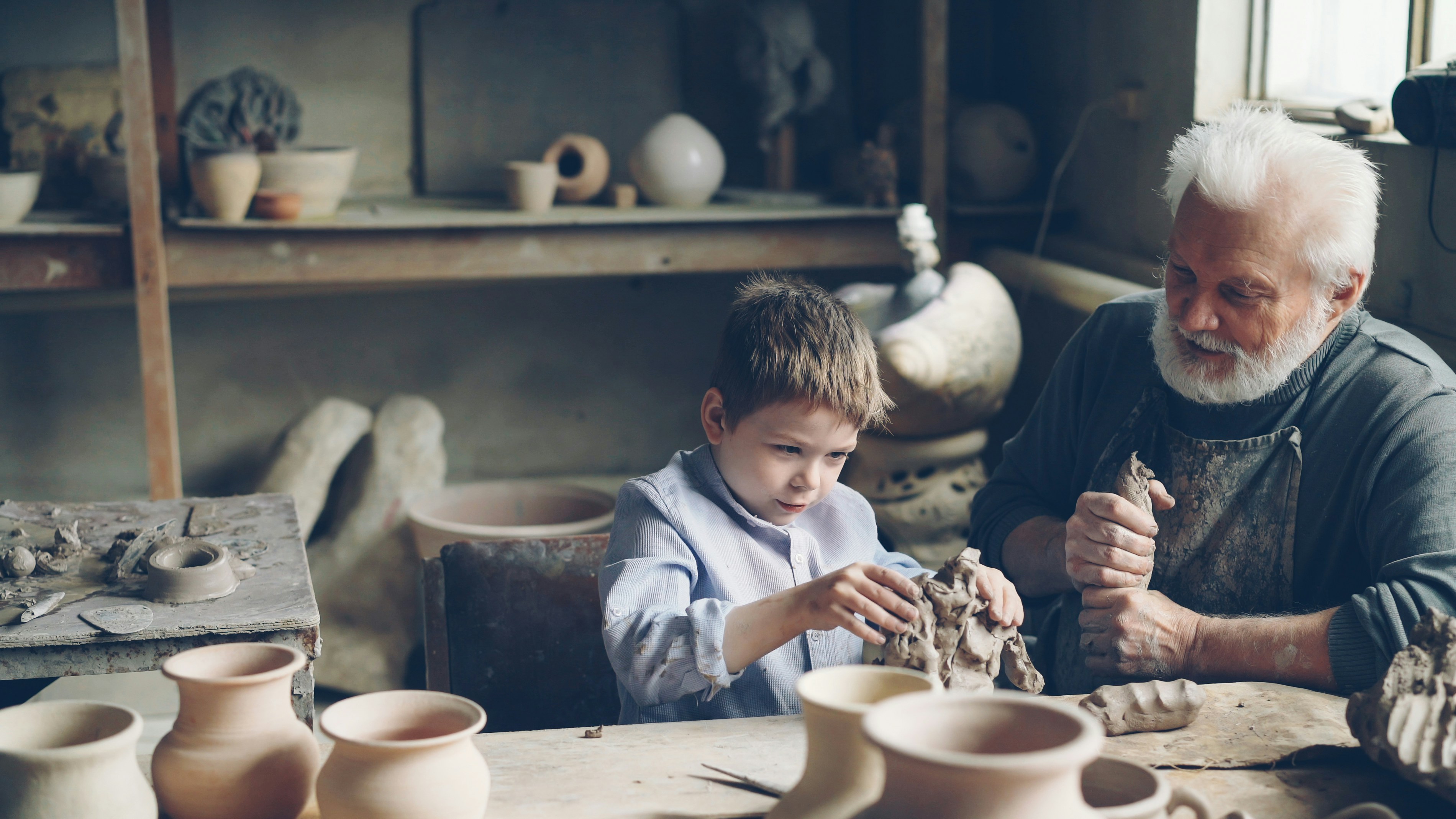 A grandfather teaches his grandson pottery skills.