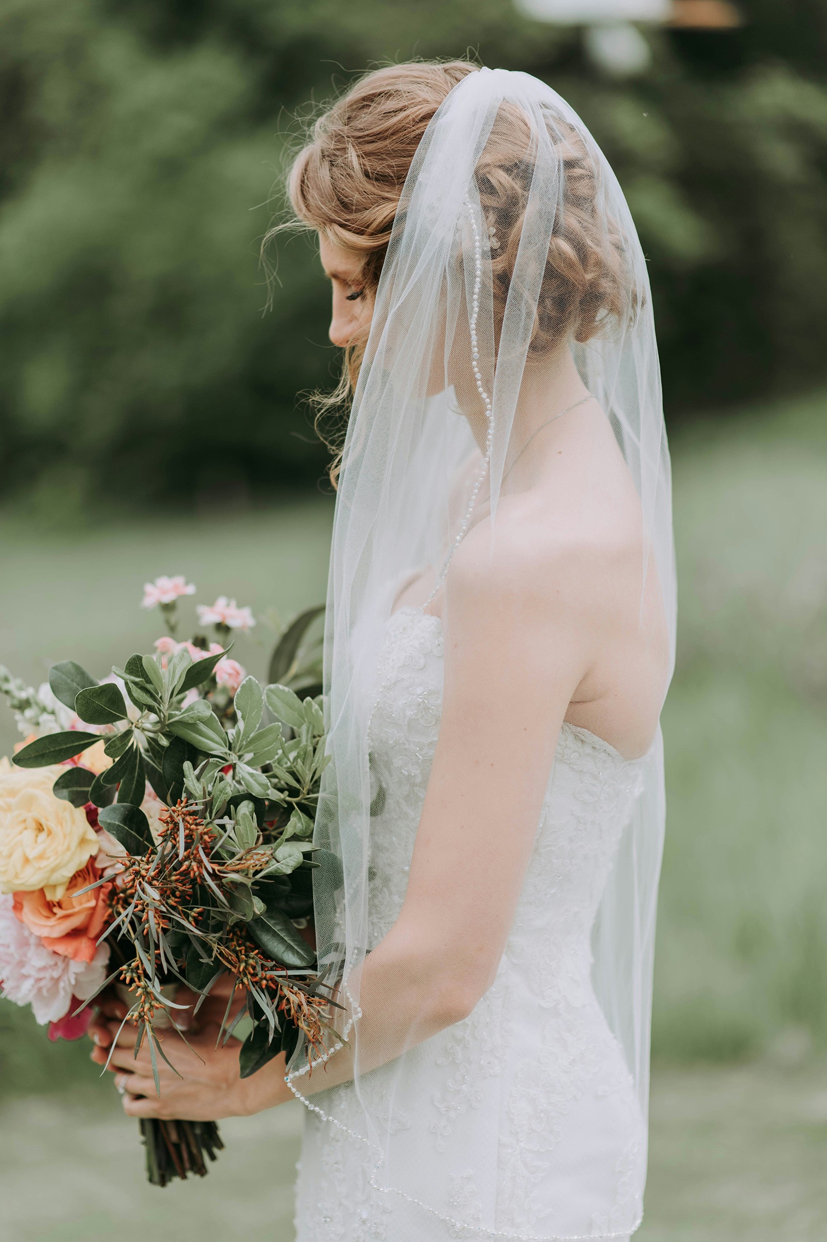 A bride in a white lace wedding dress holds a colorful bouquet of pink, yellow, and orange flowers.