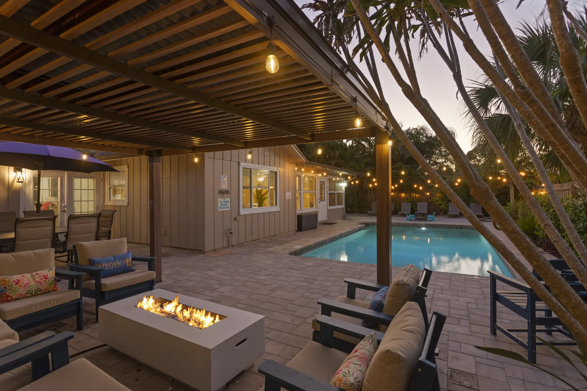 Pergola lounge around a gas fire table at dusk, with the pool beyond at Sarasota Beach Bungalow, Bradenton, Florida