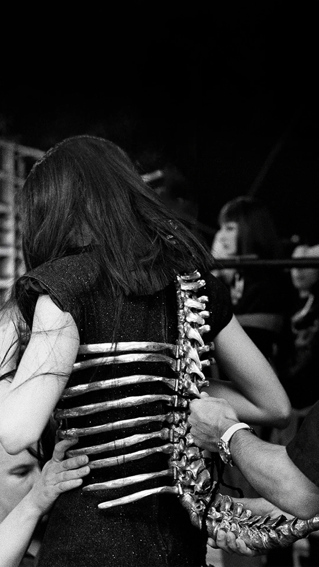 Black and white archival photo showing the fitting of the famous aluminium Skeleton Corset with a realistic spine and rib cage, designed by Shaun Leane for Alexander McQueen.