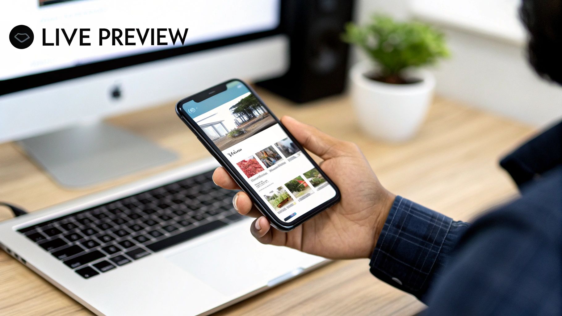 A developer testing a mobile app on a phone, with the live preview visible on a monitor behind them.