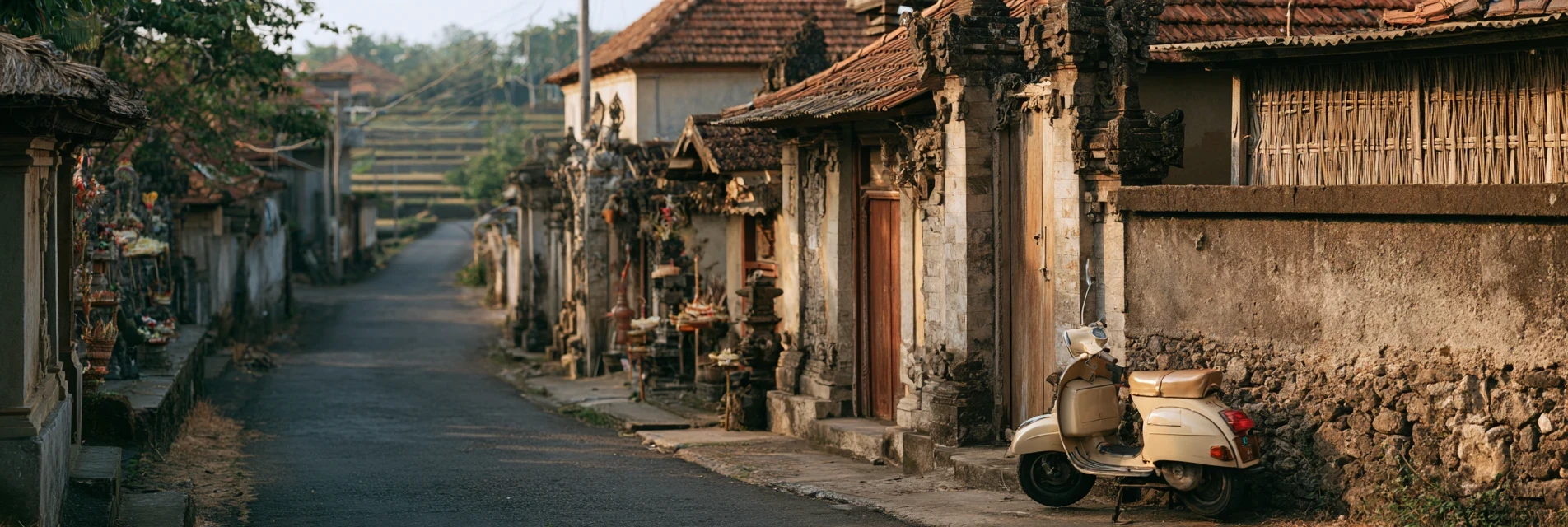 A quiet Balinese village lane at golden hour, with carved family gates, daily offerings and a vintage scooter parked against a stone wall