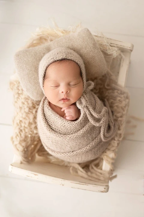 Sleeping newborn in a knit bonnet and cream wrap