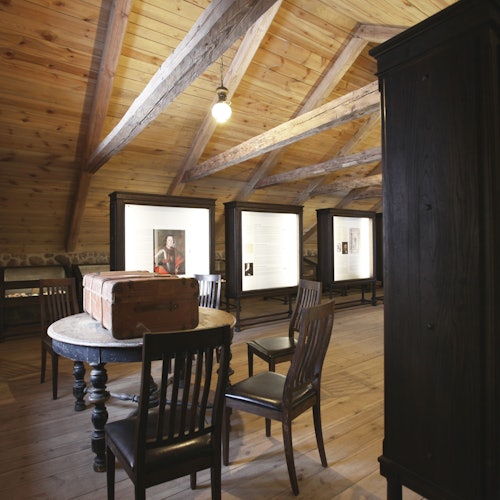 Wooden interior with a round table and chairs, showcasing framed pictures and text on easels against the walls.