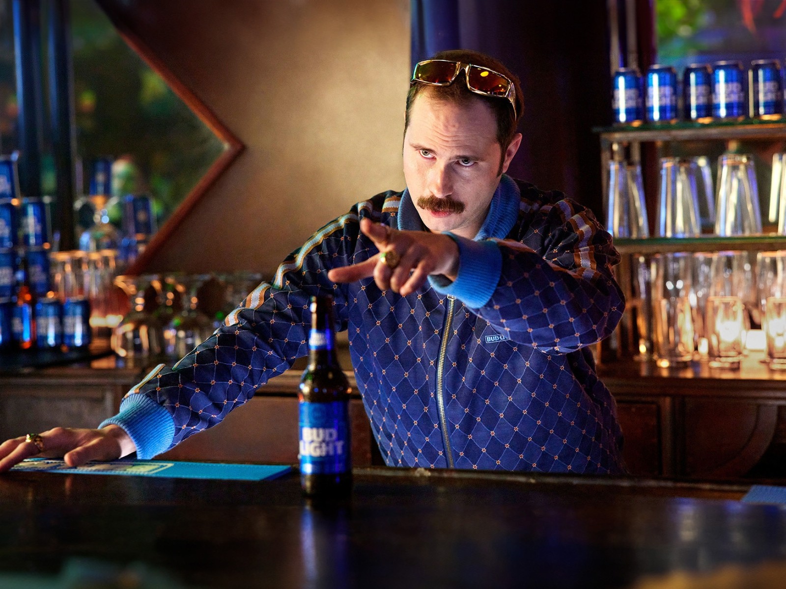 Bartender in a patterned shirt working behind a bar counter with illuminated bottles visible in the background, capturing the ambiance of an upscale venue.
