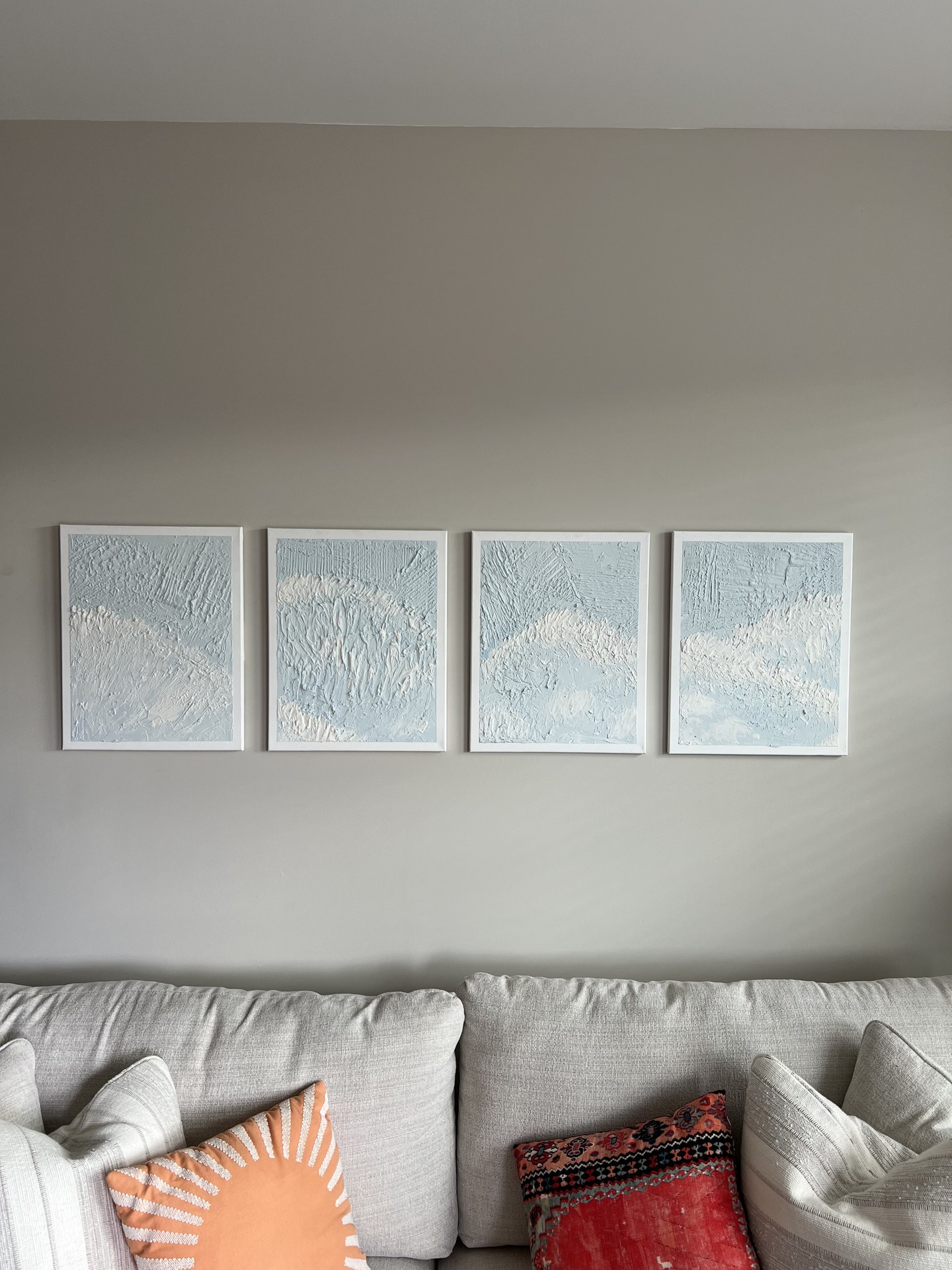 Four pale framed panels aligned above a sofa.