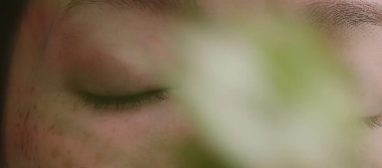 A mother’s face at rest, eyes closed, behind soft greenery
