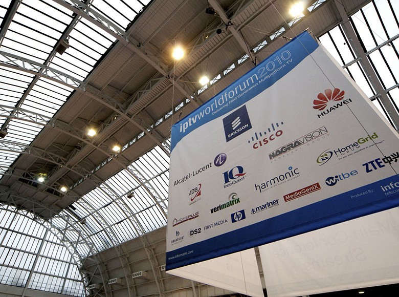 Large cubed event signage with sponsor logos hanging from an exhibition ceiling.