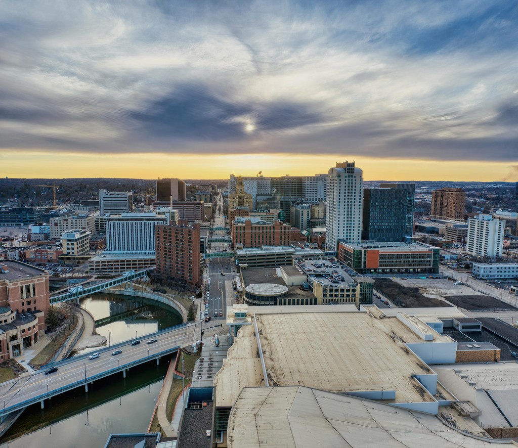 Aerial view of a cityscape with tall buildings, a river, and a bridge at sunset.