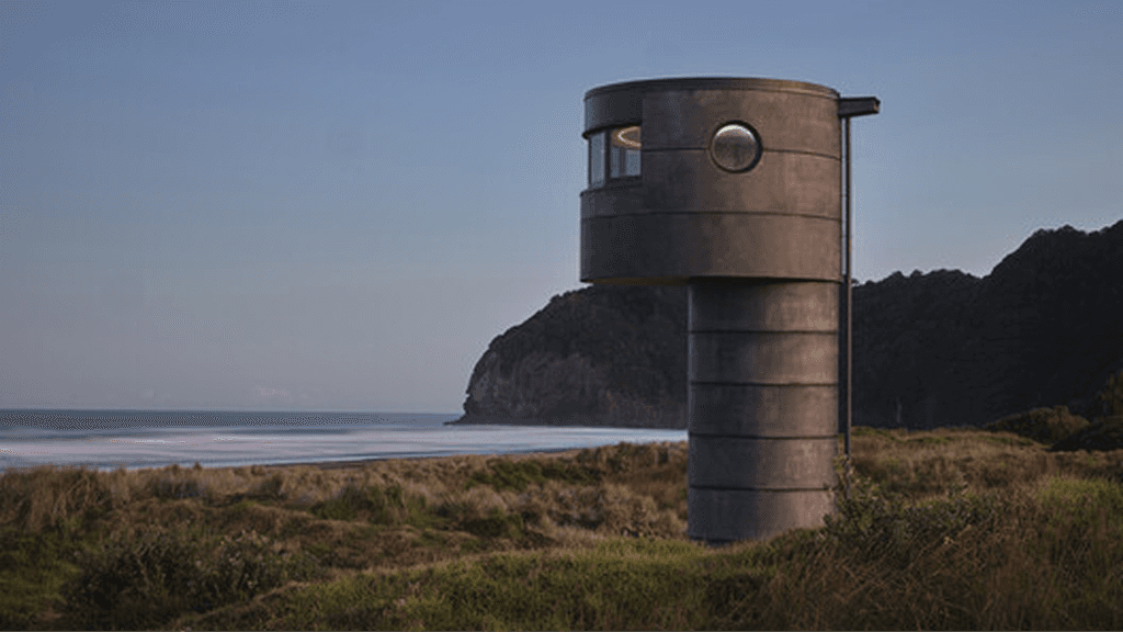 Cylindrical concrete tower on a grassy coast overlooking the ocean and distant hills.