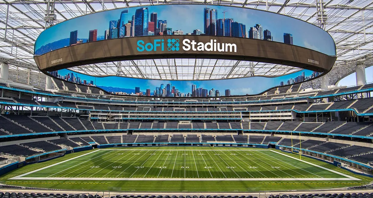 Interior view of SoFi Stadium with the field and seating bowl visible beneath the curved digital scoreboard.