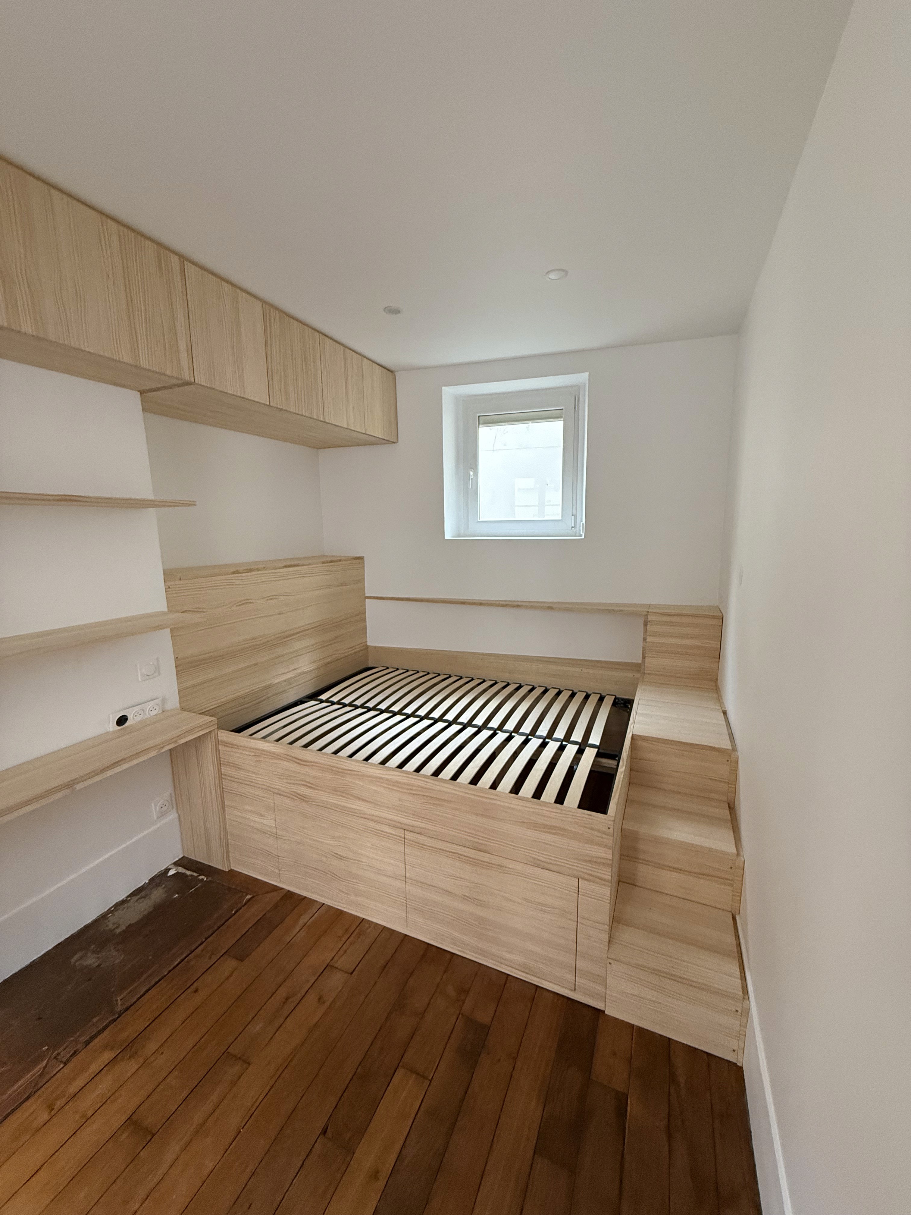 Aménagement global d'une petite chambre avec lit surélevé, bureau intégré et étagères artisanales en bois.