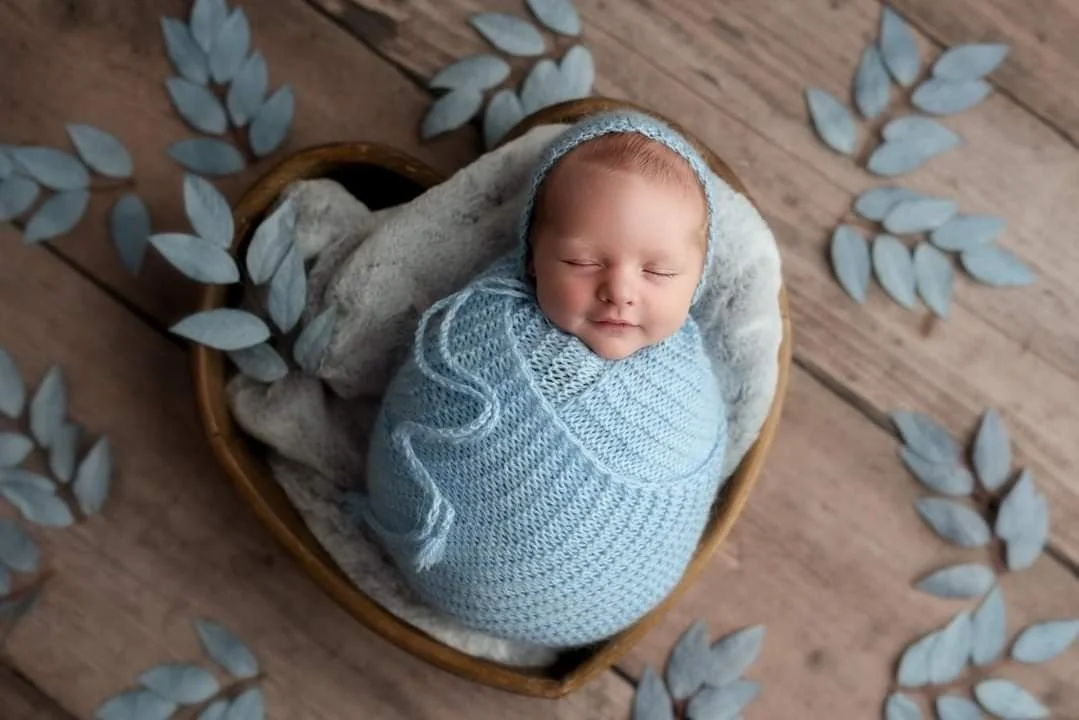 Newborn in a blue wrap in a basket with eucalyptus leaves