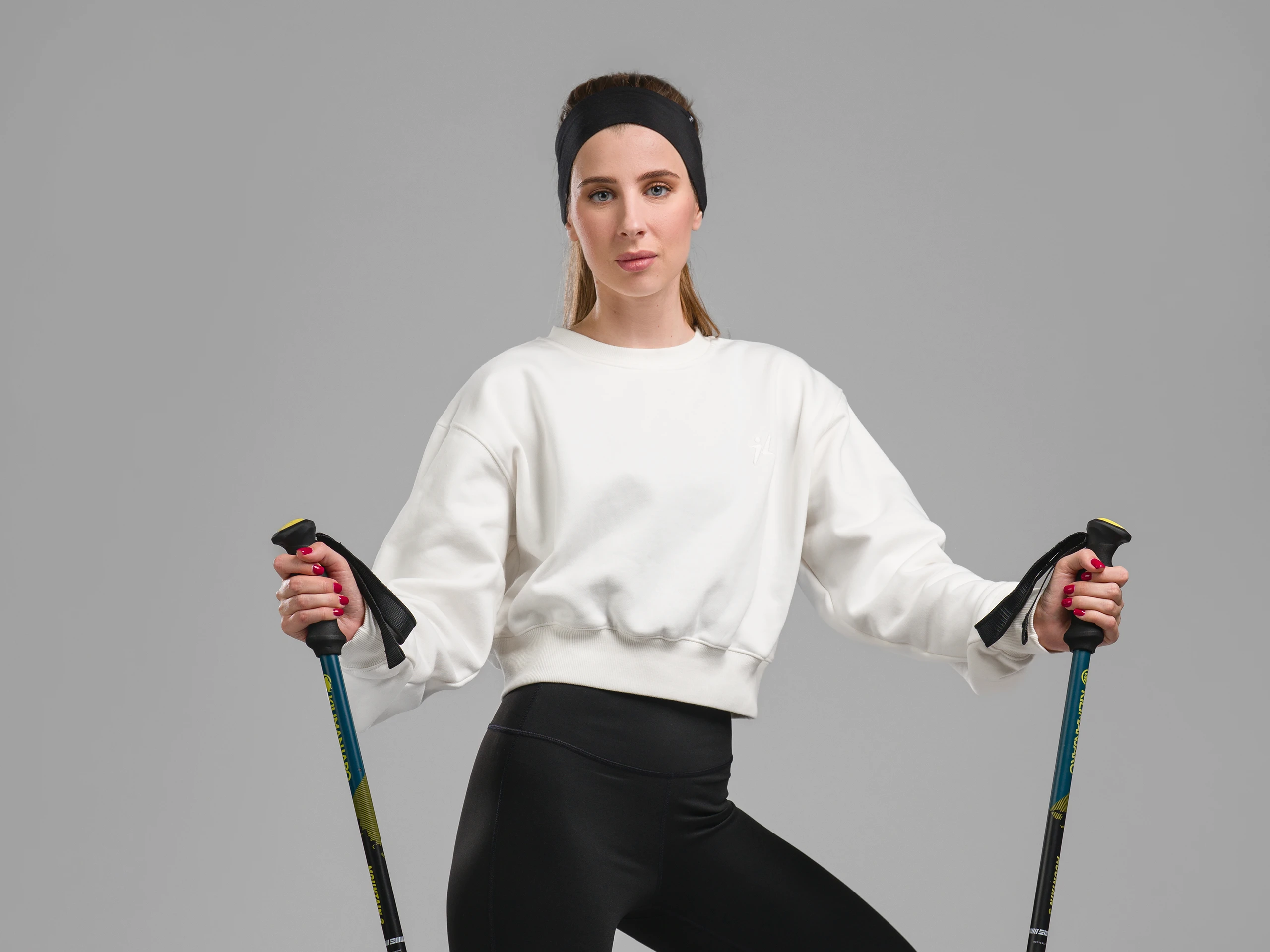 Woman in sportswear holding trekking poles, standing in a studio on a light background.