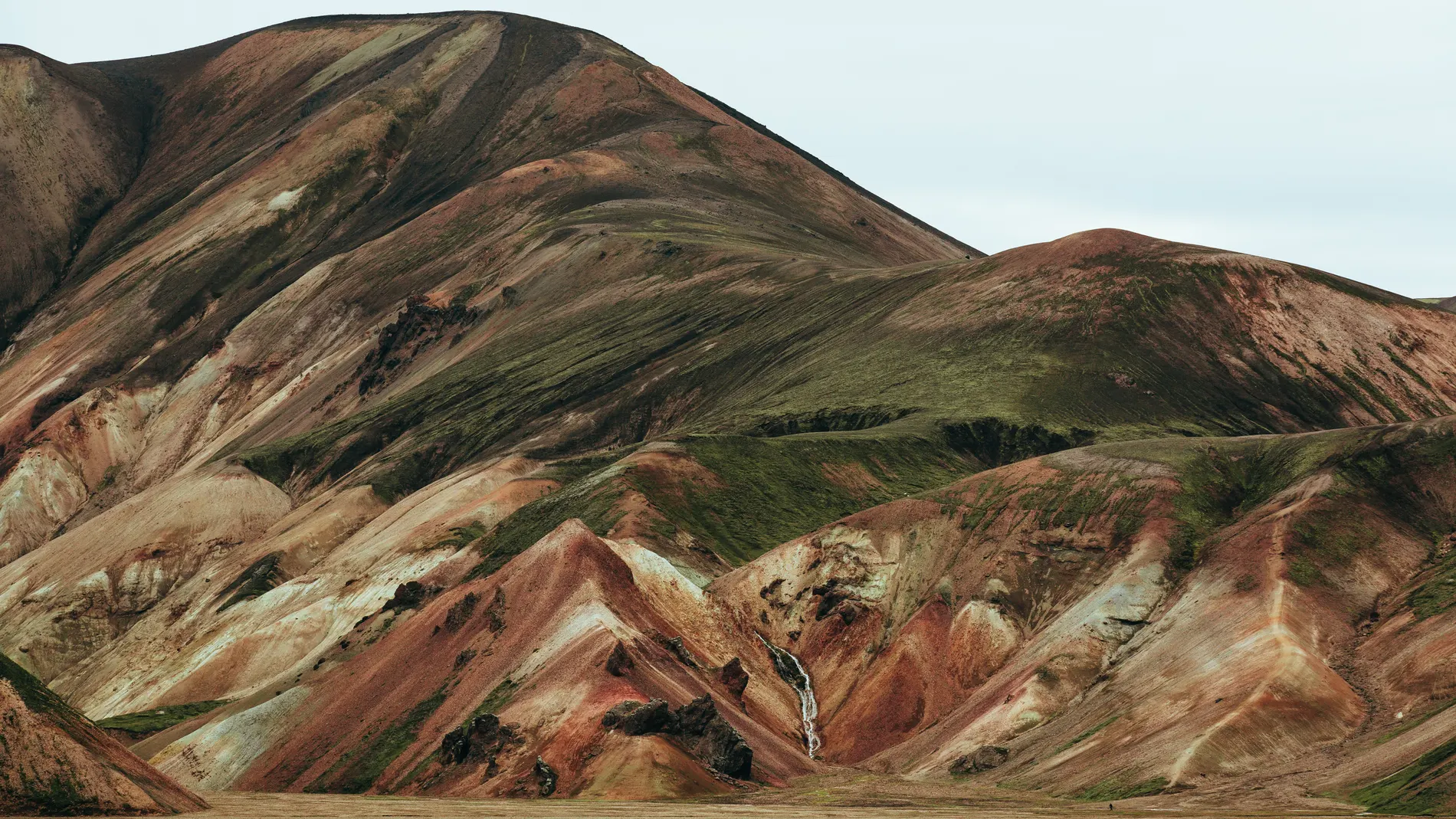 A mountainside banded with ochre, green and rust-coloured mineral streaks