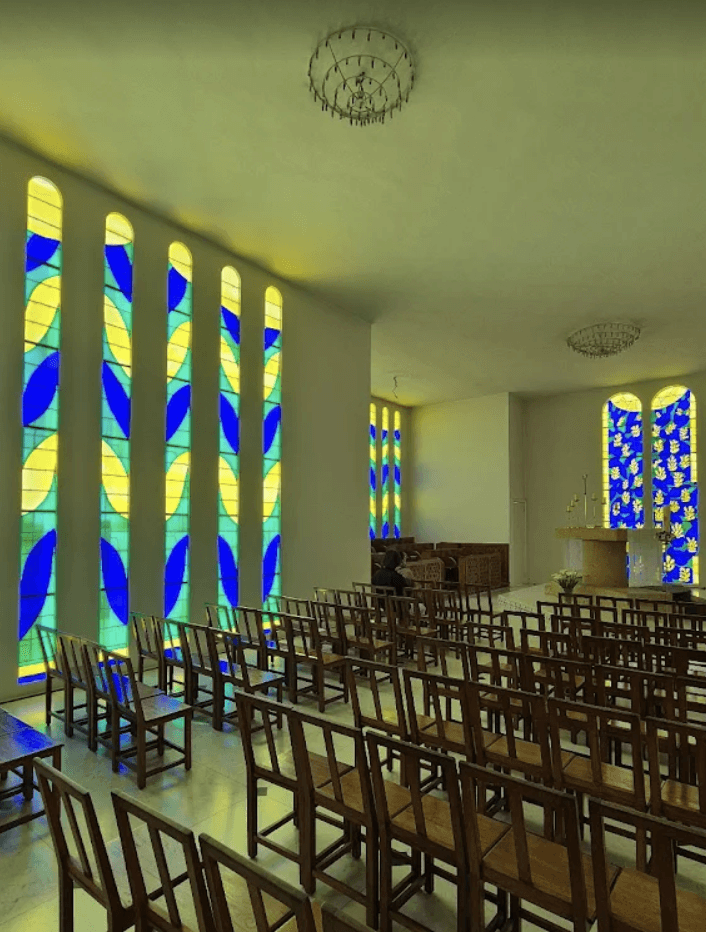 Interior of the Chapelle du Rosaire in Vence, France, with Henri Matisse’s blue, green and yellow stained‑glass windows and wooden chapel chairs.