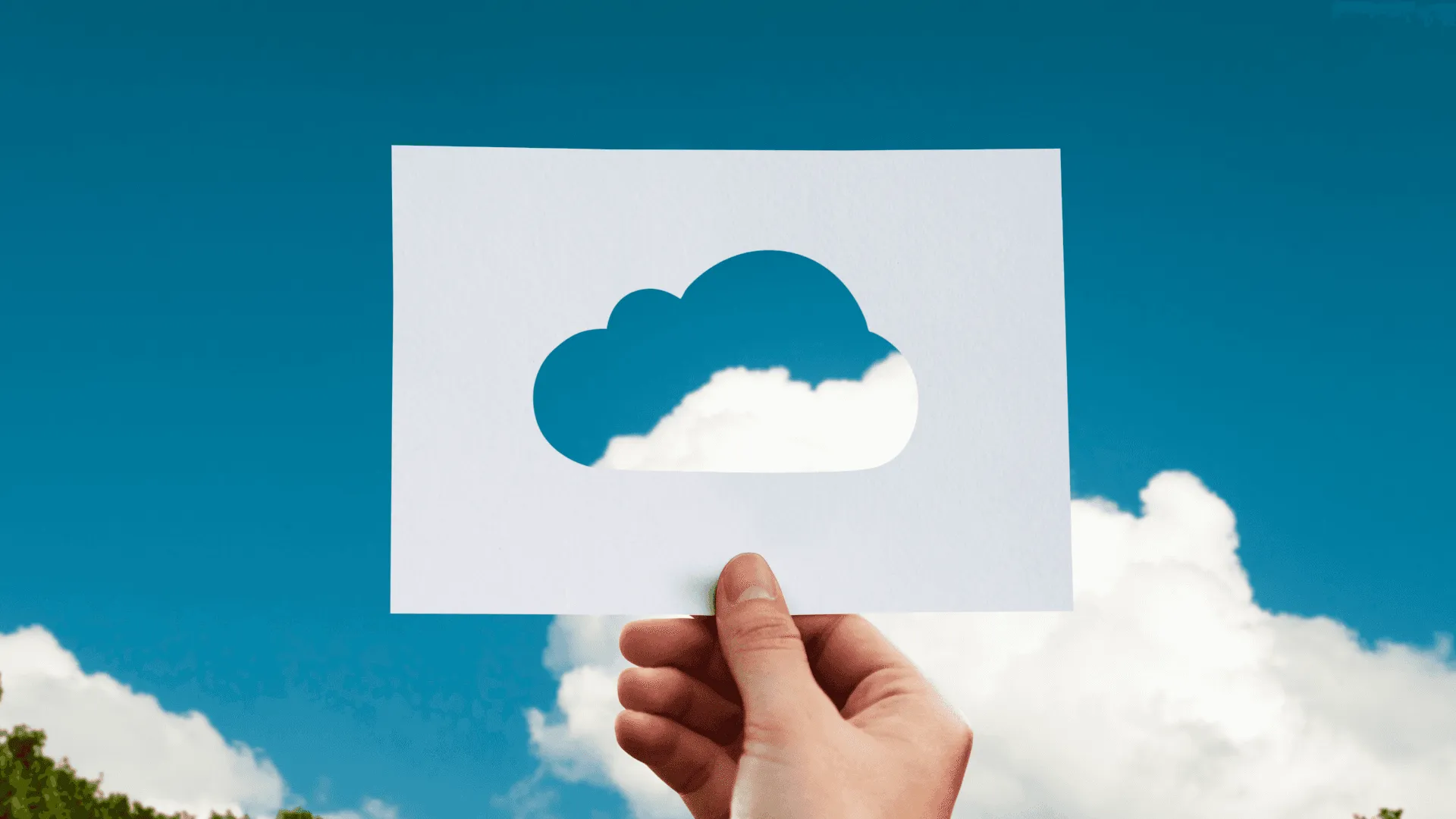 A piece of paper with a cloud cut out being held up to a blue sky with white clouds