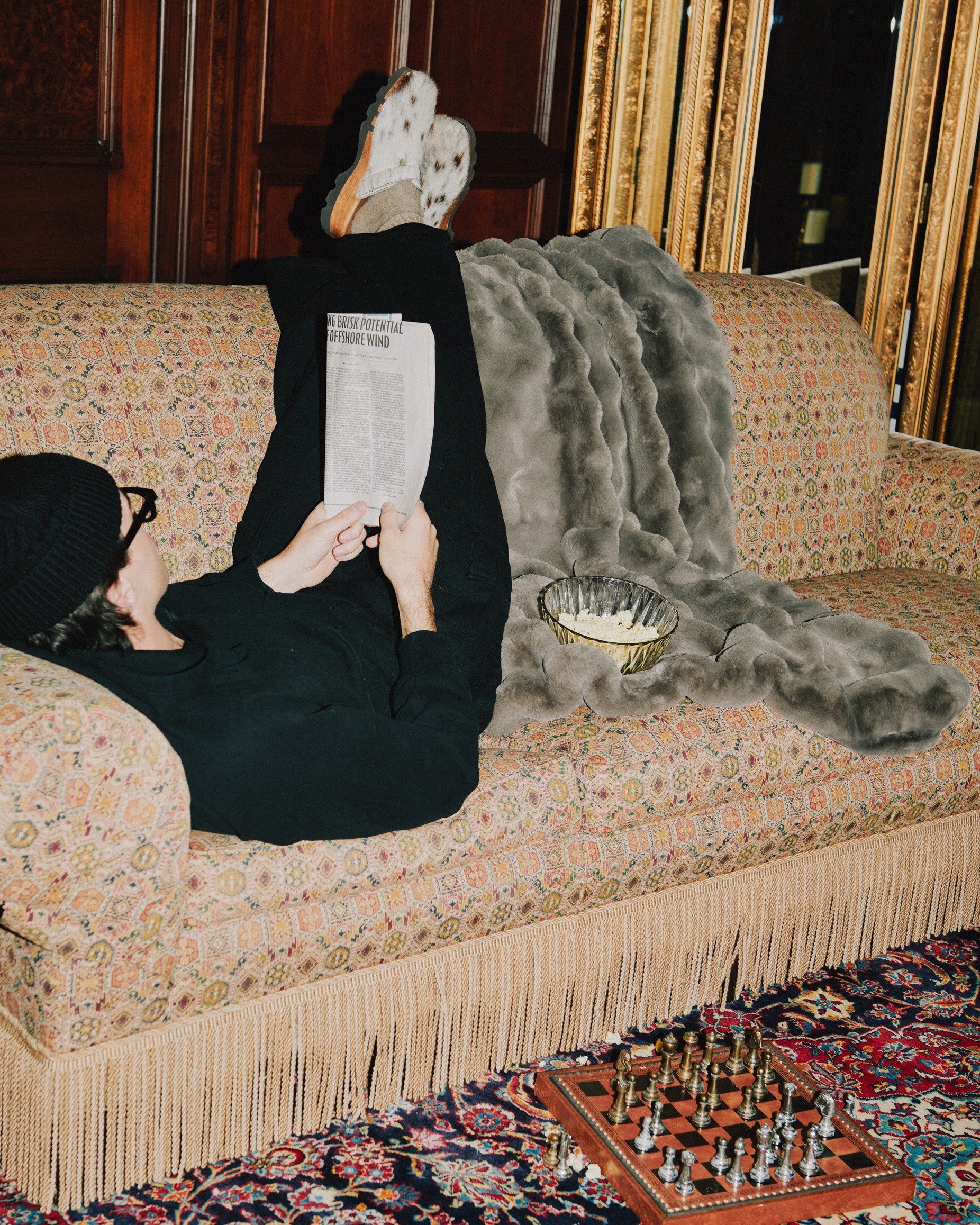 A soft cream-colored Normy blanket with a visible brand label is draped inside a decorative bathroom sink. The scene also includes bath products around the sink and a mirror reflecting the cozy setup, creating a playful and inviting atmosphere.