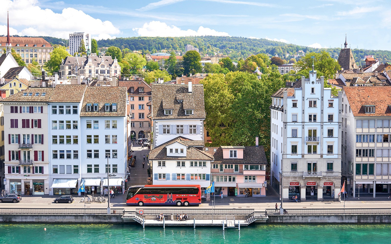 취리히 리마트 강을 따라 늘어선 역사적인 건물들, 가까운 곳에 주차된 투어 버스가 있습니다.