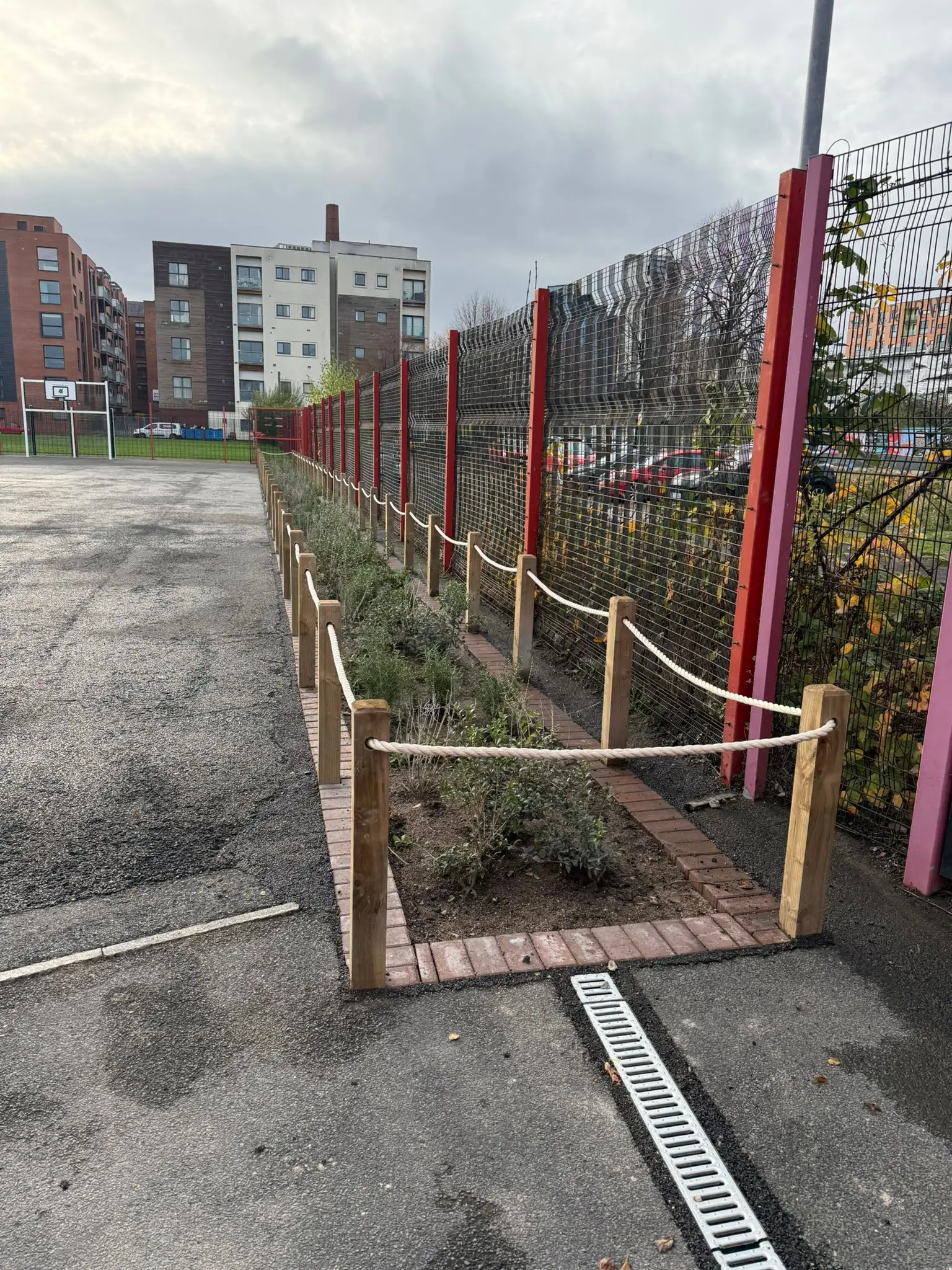 A fenced garden area in an urban setting, with buildings visible in the background under a cloudy sky.