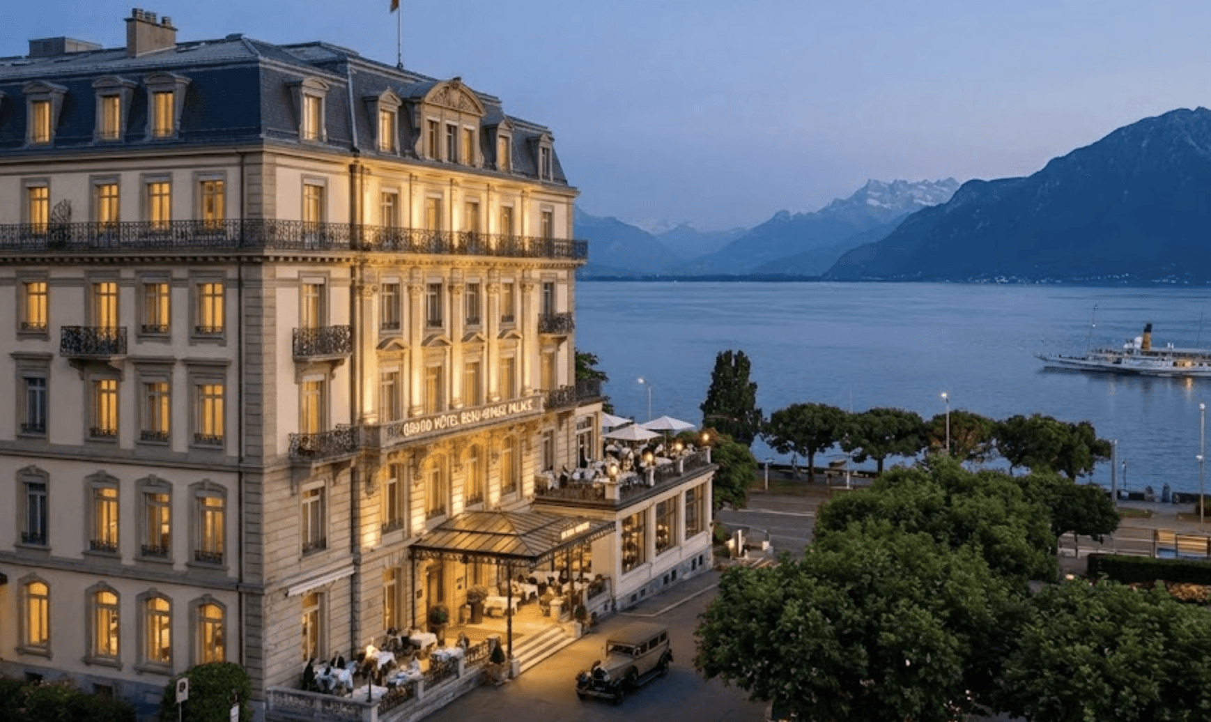 An elegant, multi-story luxury hotel situated on a scenic waterfront, perfectly optimized for hotel SEO services to highlight its premium amenities, classic European architecture, and breathtaking views of a mountain-lined lake at dusk.