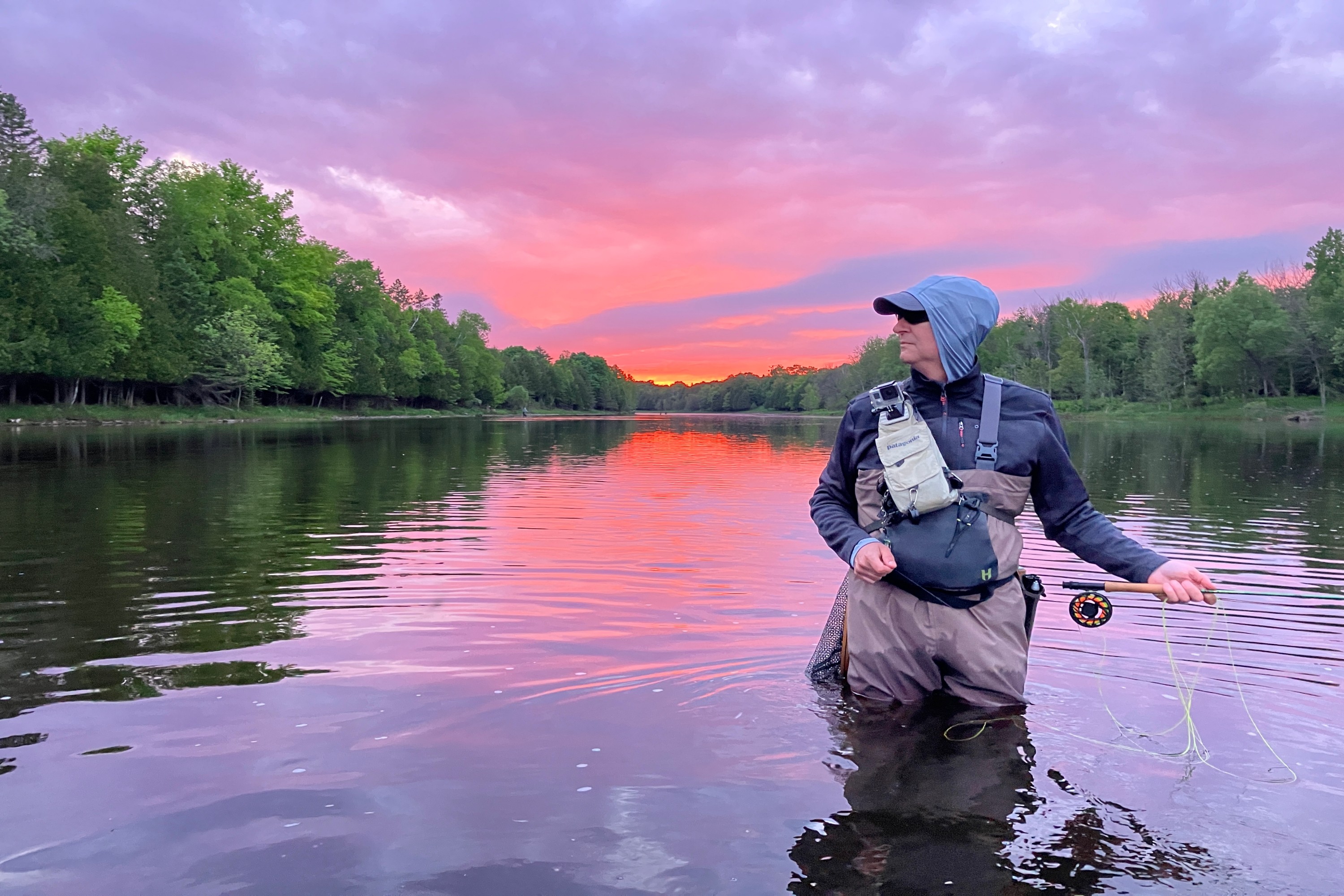 Fly fisher standing in the river beneath a pink sunset