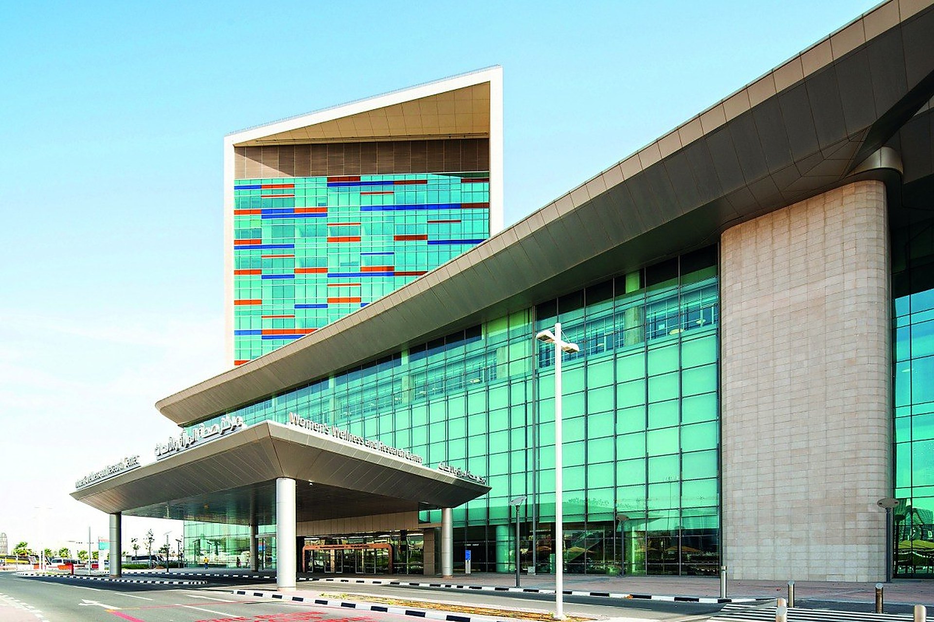 L'entrée de la maternité publique Women's Wellness and Research Center, à Doha, avec sa façade de verre et sa tour colorée, où l'on accouche avec la carte santé