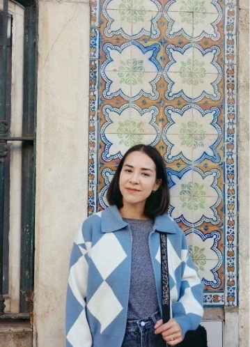 Caro smiling in a warm, outdoor setting with soft sunlight and a wall of painted Portuguese tiles in the background.